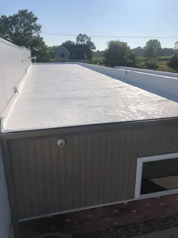 White flat roof on a building with brown siding, sunny outdoor setting.