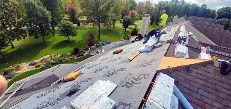 Roofers working on a roof, installing shingles.