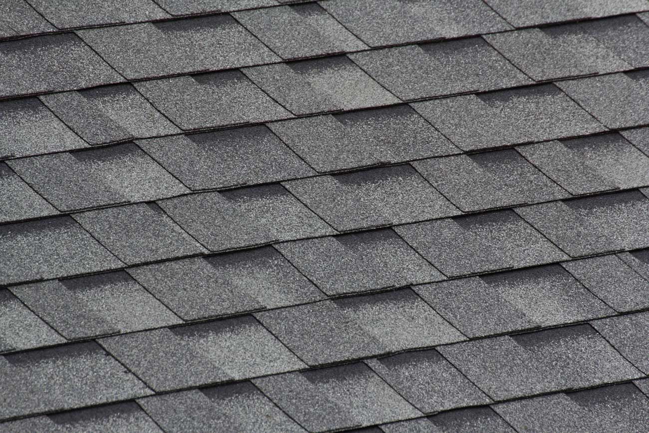 Close-up of gray asphalt roof shingles in diagonal layout on residential home roofing surface.