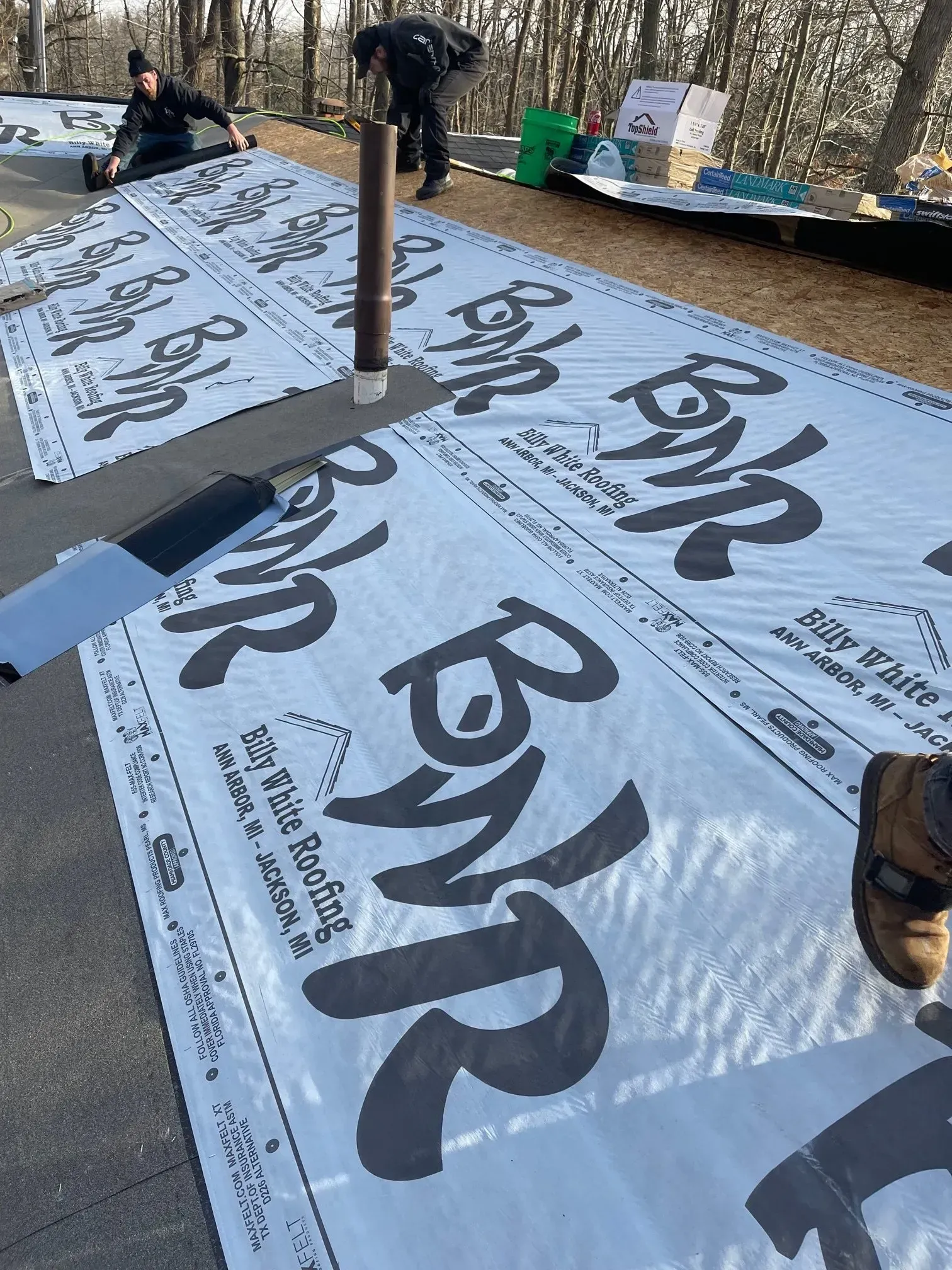 People installing roofing material, featuring large black text BWR on white rolls outdoors.