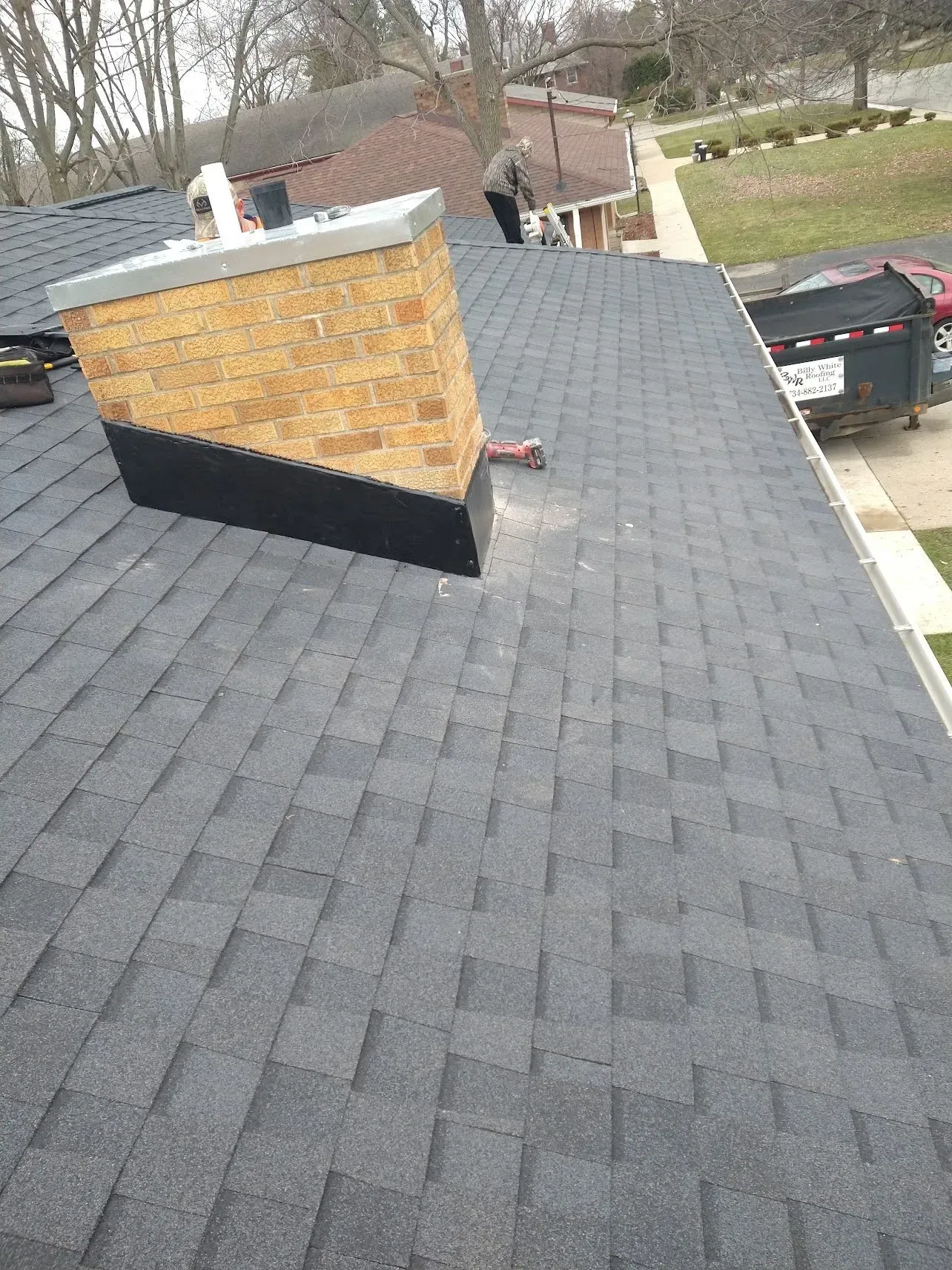 Dark gray shingle roof with a brick chimney and a black base.