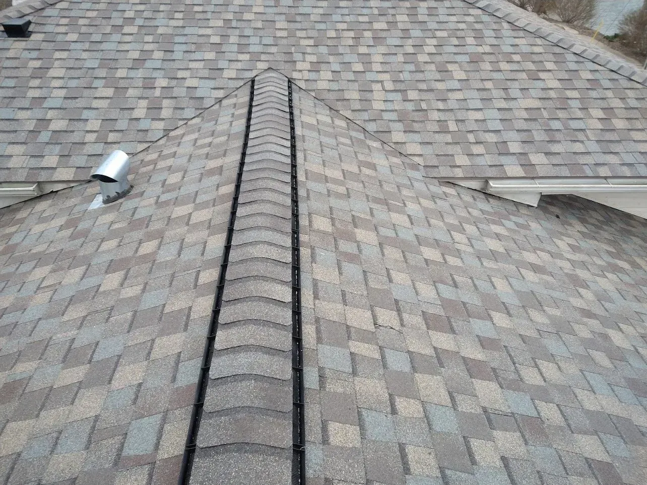 Overhead view of a roof with brown and gray shingles and a dark ridge.
