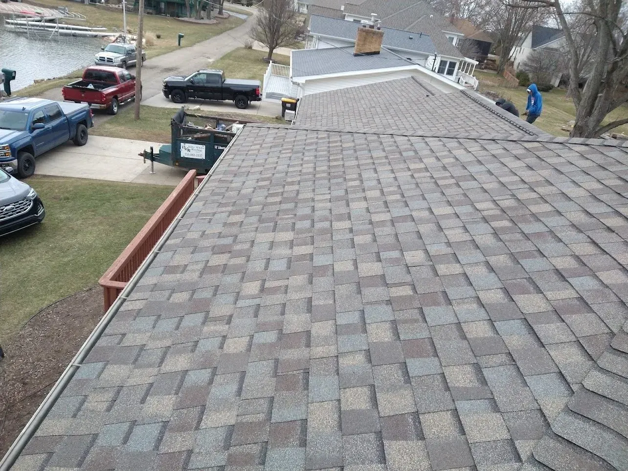 A multi-colored shingle roof of a house with lake and vehicles visible in the background.