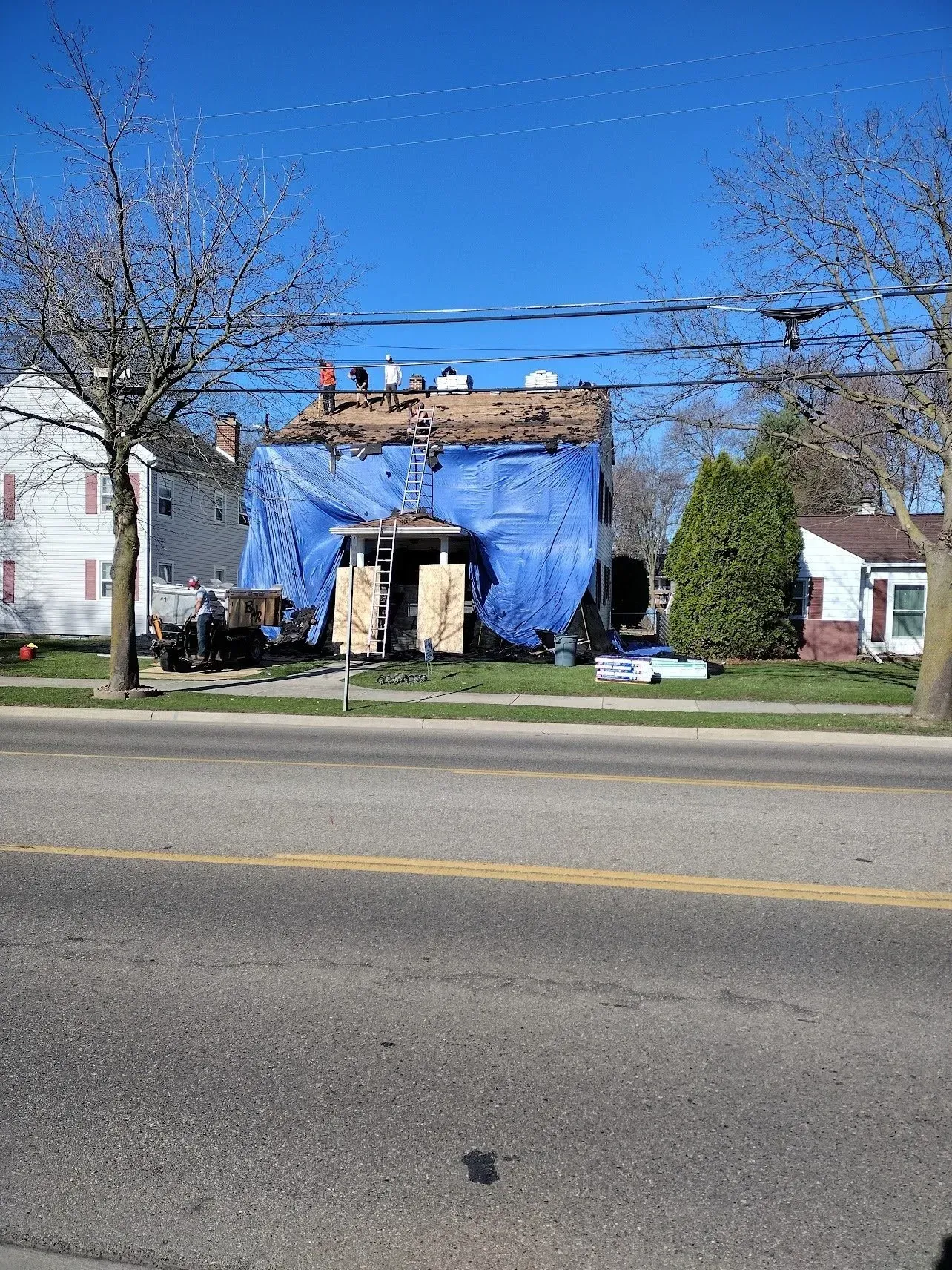House under construction, covered in blue tarp, with exposed roof.