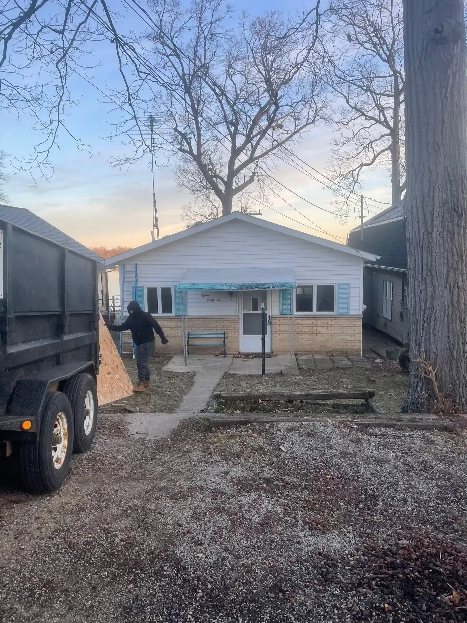 Gray gravel yard, trees in the background, a trailer on the left.