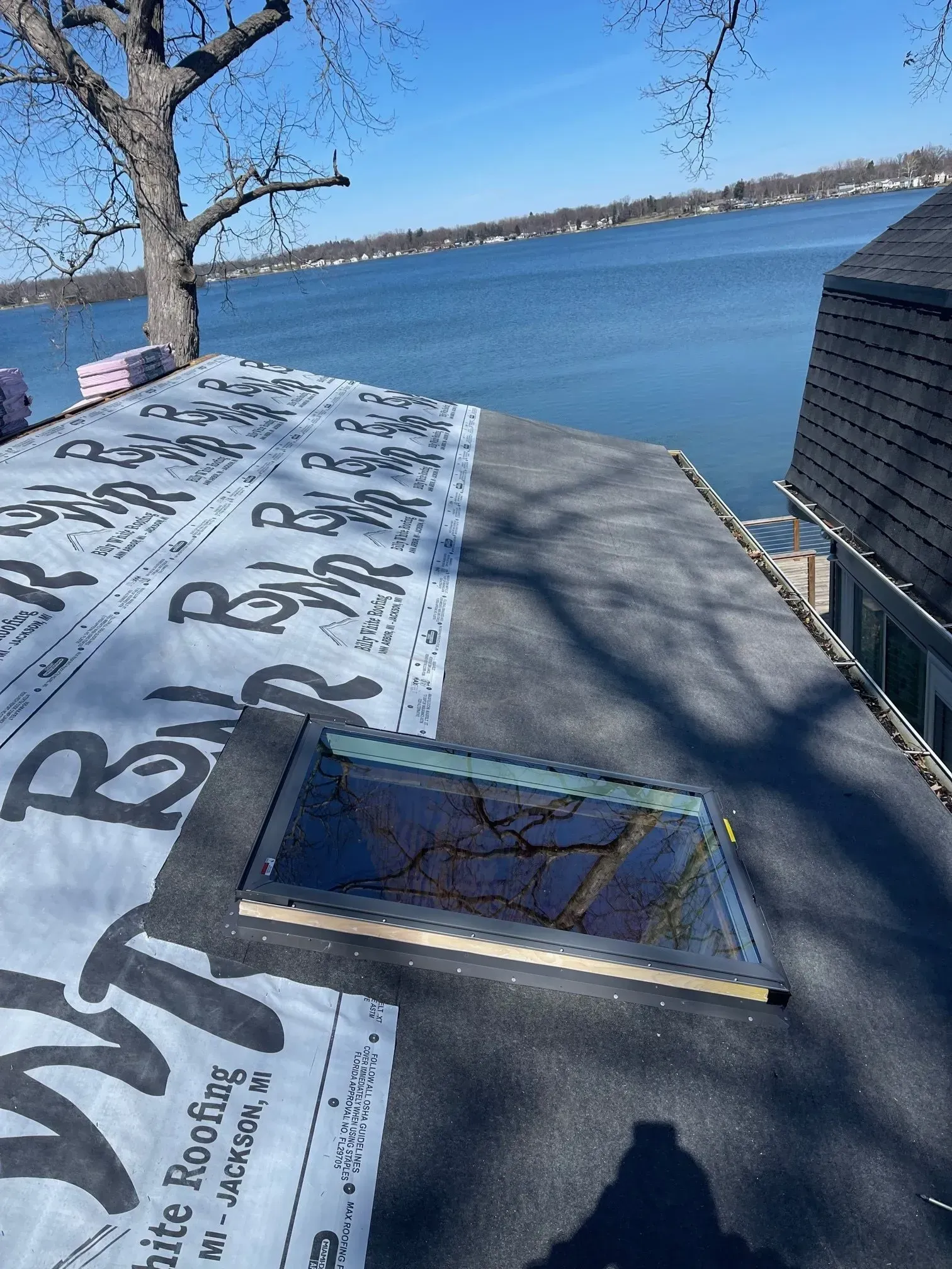 Roof repair with partial roofing material laid, skylight, lake view.