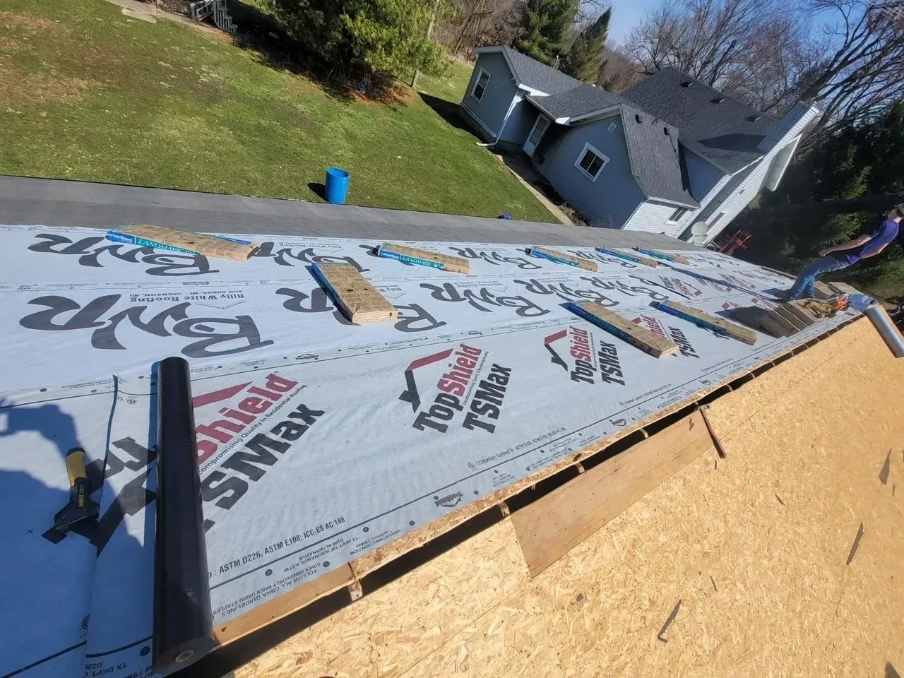 Roofers installing roofing material on a house, with blue tarp in the background.