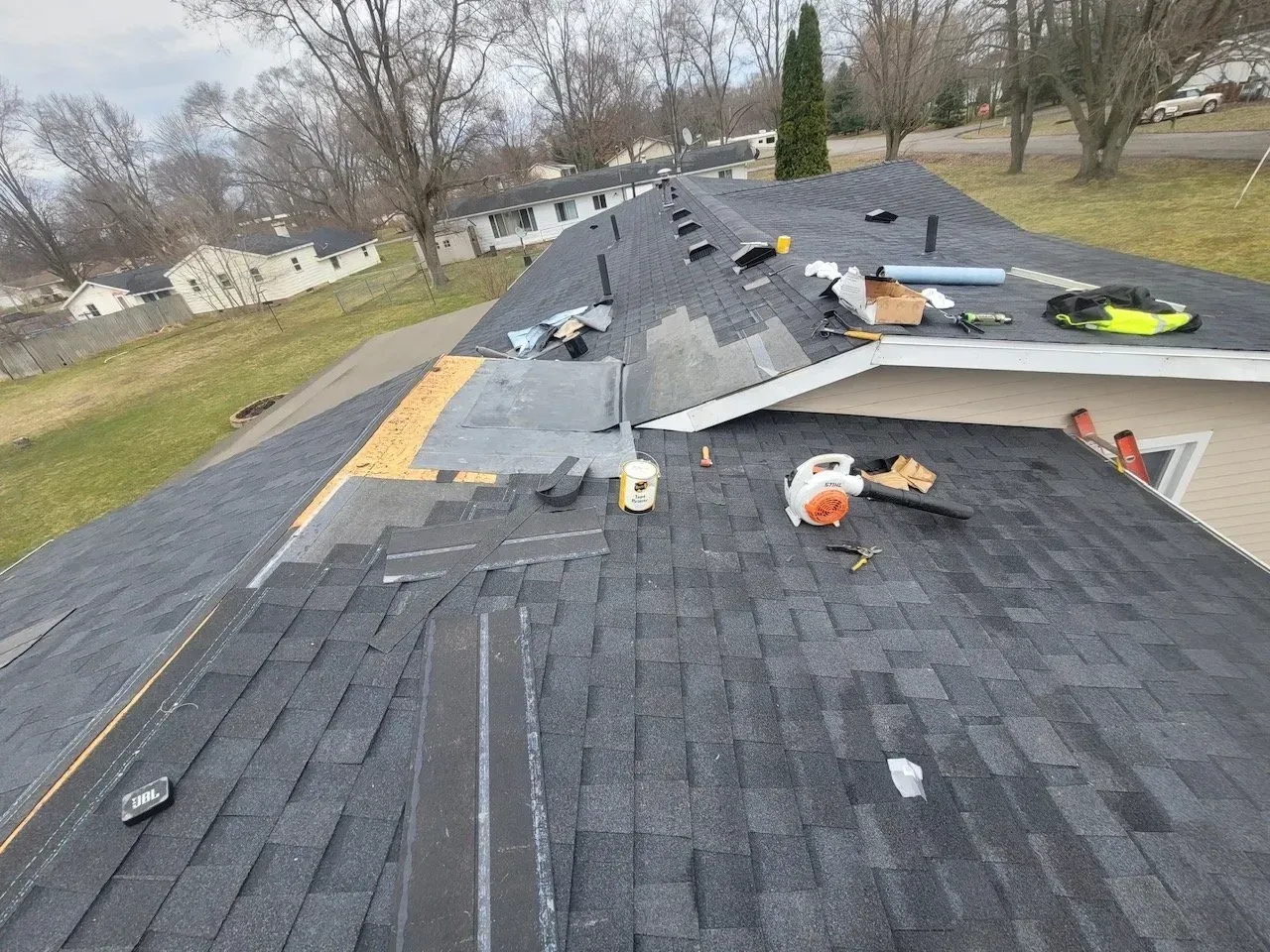 Gray shingles, tan underlayment, and a leaf blower are visible.