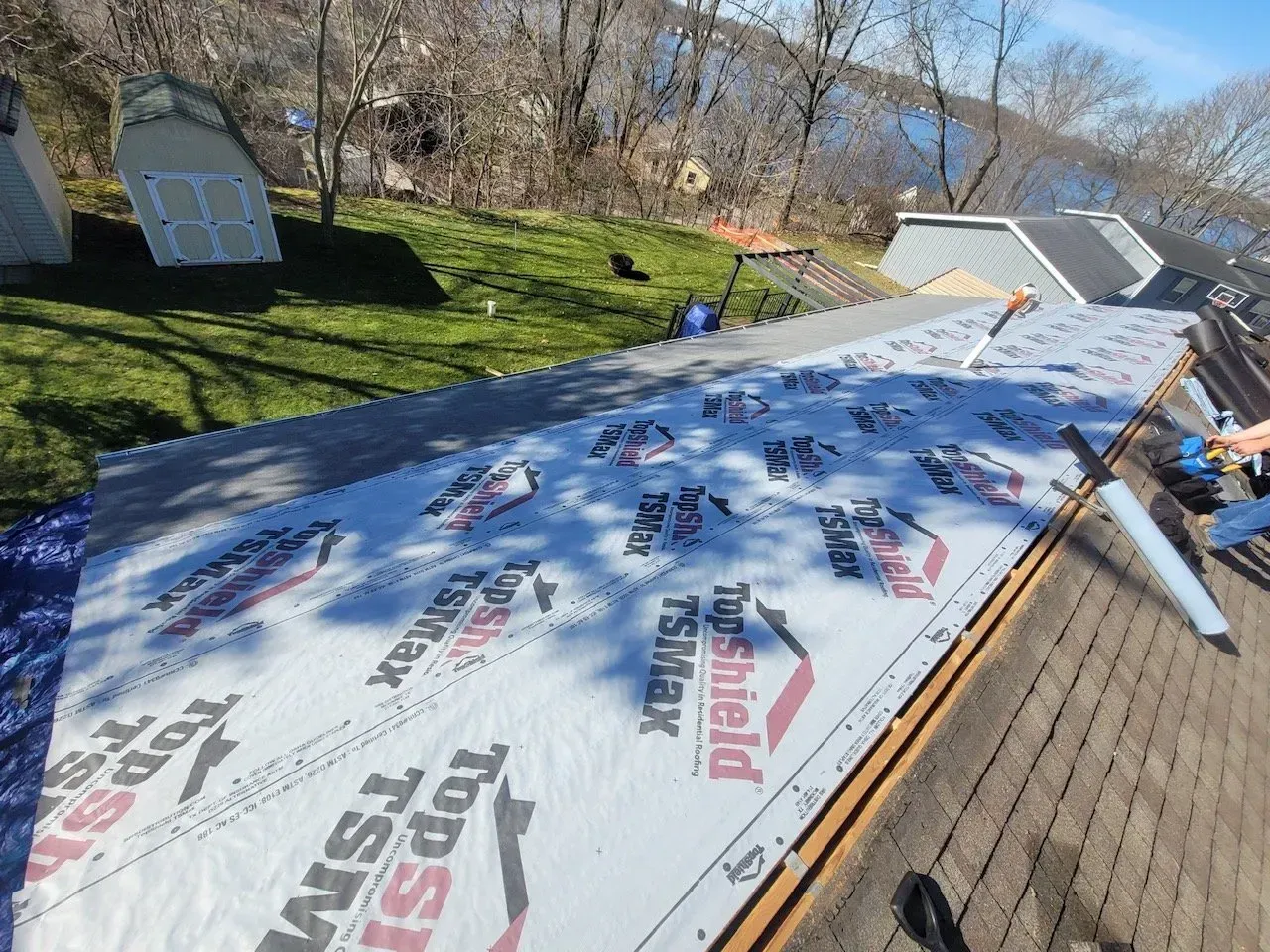 Roof being repaired with new underlayment, showing a partially replaced roof in a yard near water.