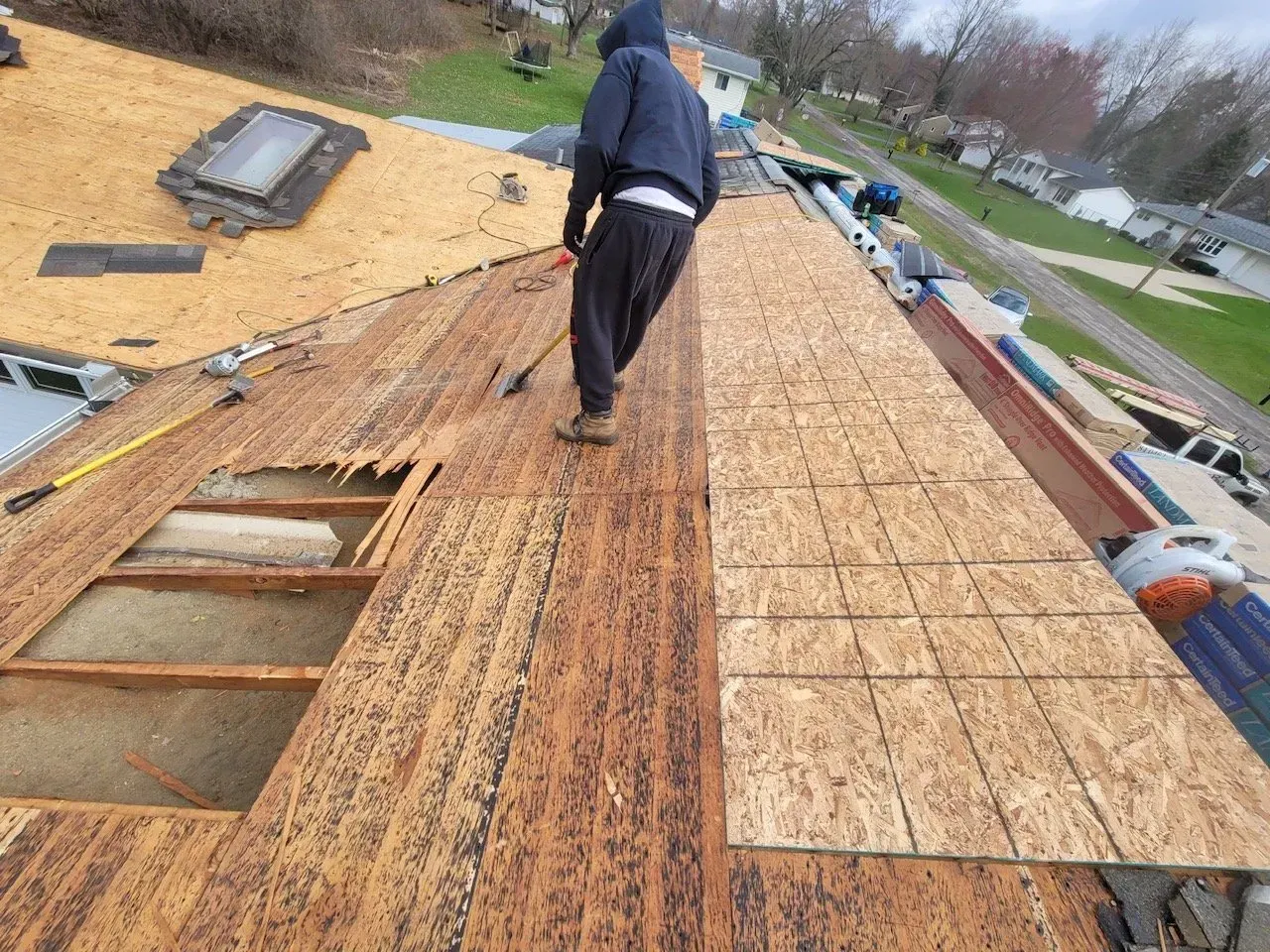 Man on a damaged roof replacing wood panels.