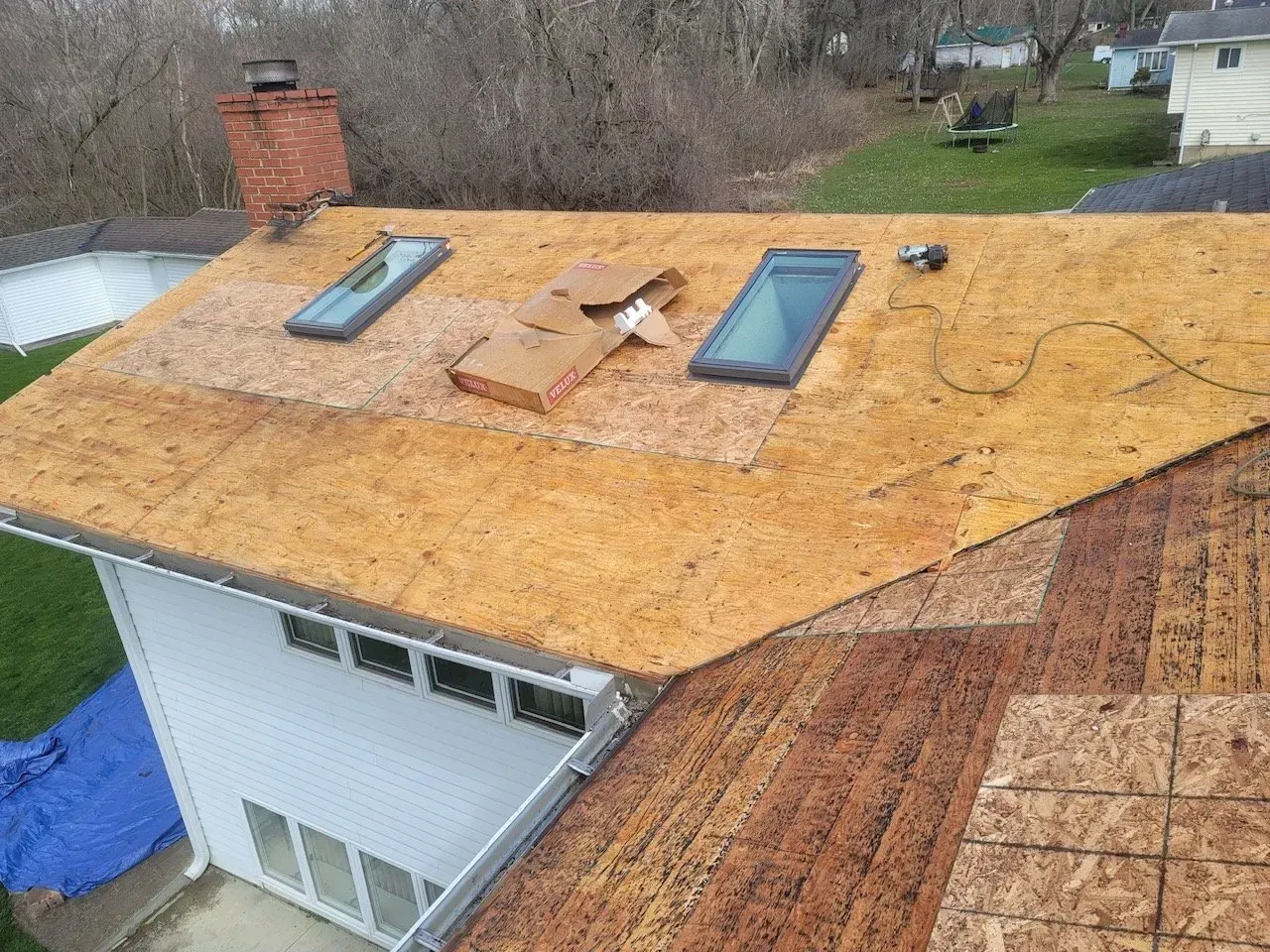 Rooftop with skylights and exposed wood, partially covered with new sheathing.