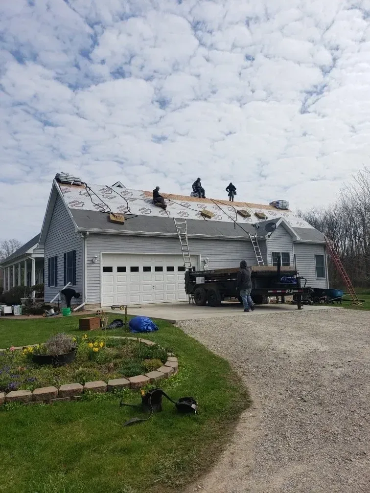 Roofers working on a residential roof, with materials and a truck present on a cloudy day.