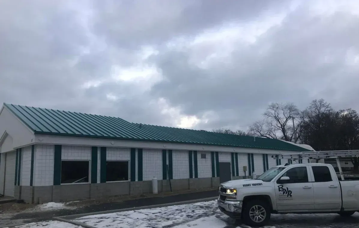 White truck parked outside a building with a green roof, windows, and cloudy sky.