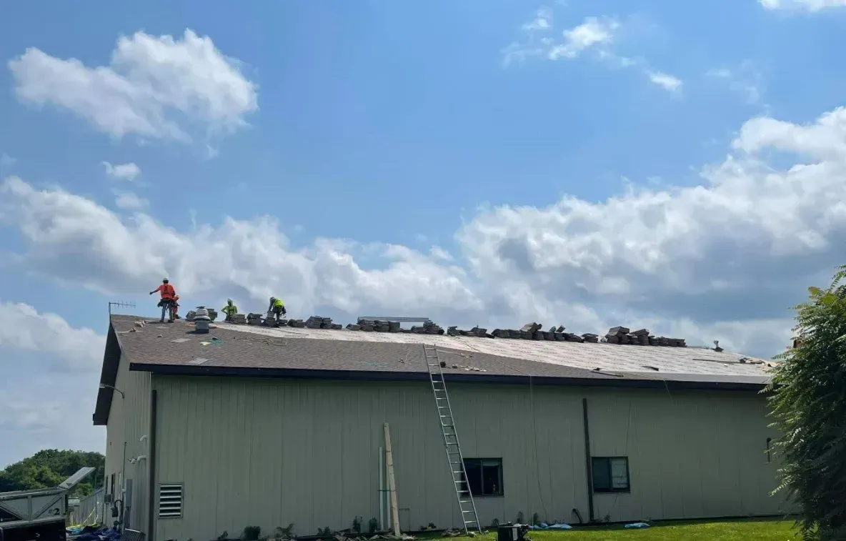 Roofers in safety vests working on a building's roof under a cloudy sky.