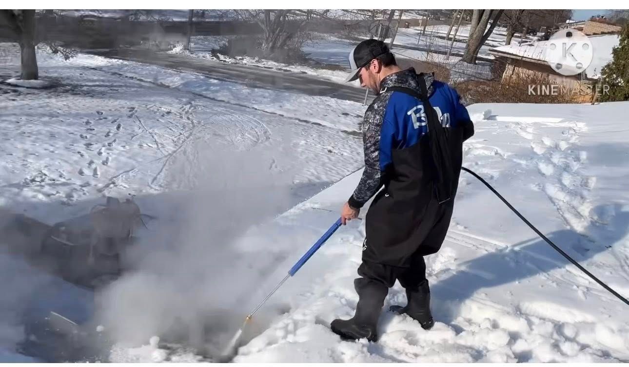 Man using a pressure washer on a snow-covered roof, steam rising.
