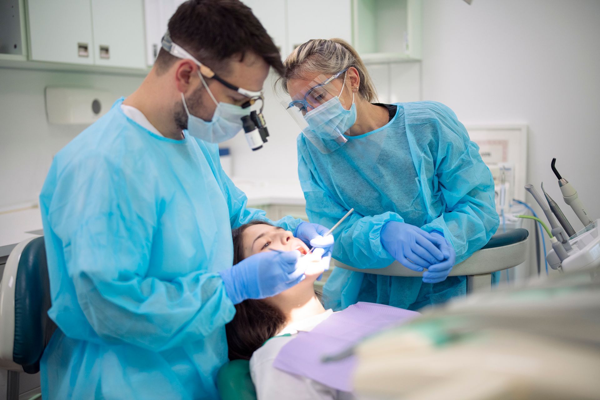 Dentist examining a patient's teeth with an assistant in a dental office.