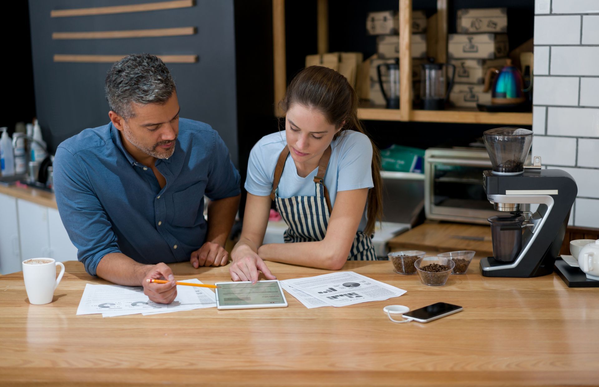 Man and woman reviewing papers and tablet at coffee shop counter.