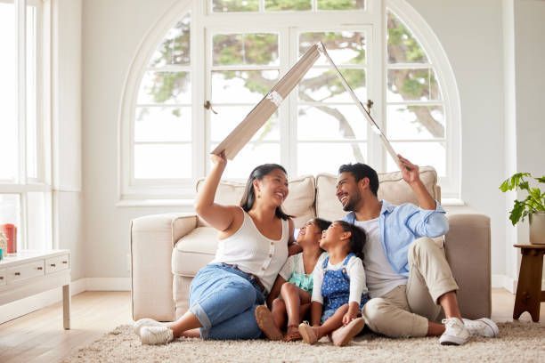 Family sitting in a living room, smiling, holding a cardboard roof above their heads.