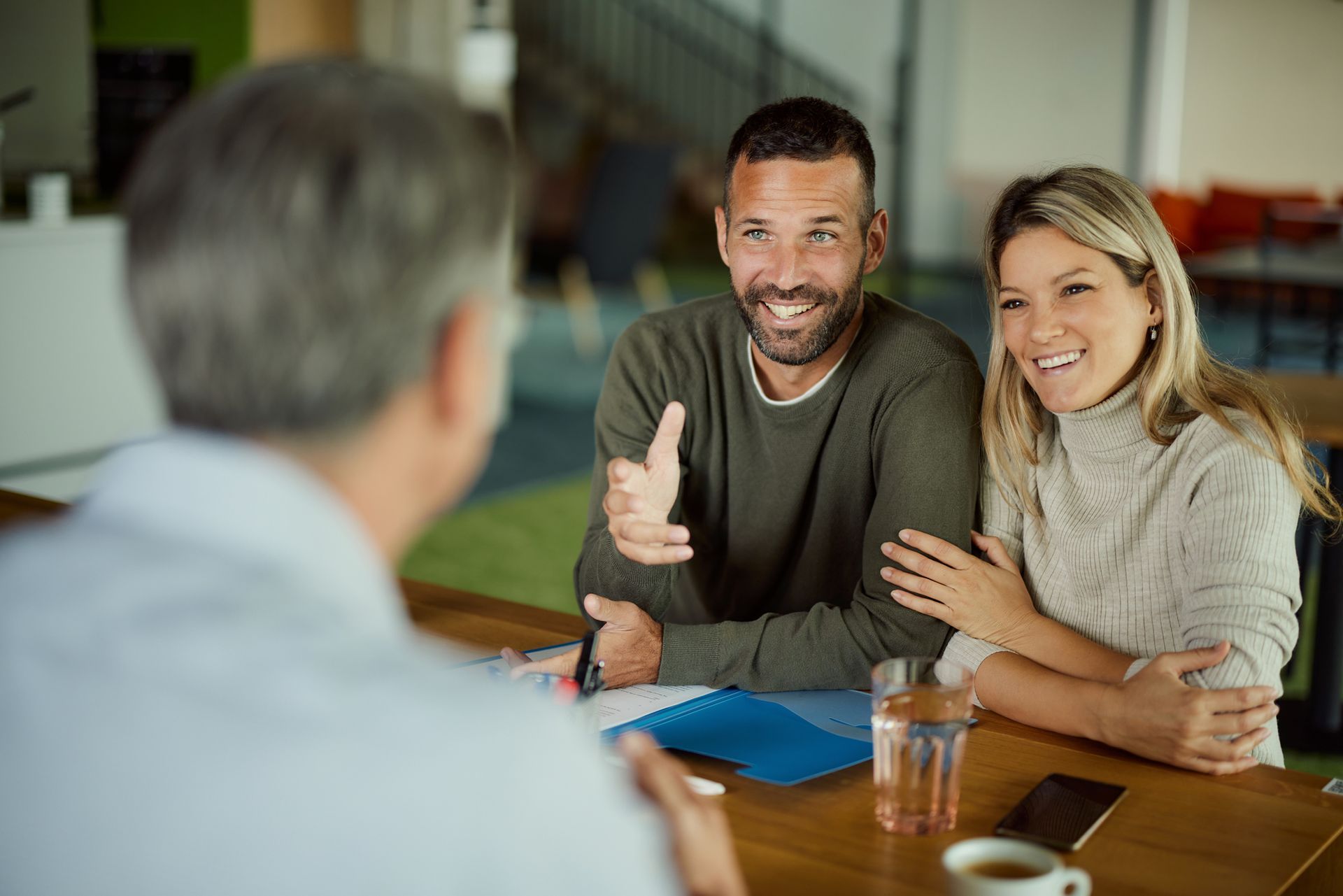 Couple smiling, talking with a person, seated at a table, blue folder, glass of water.
