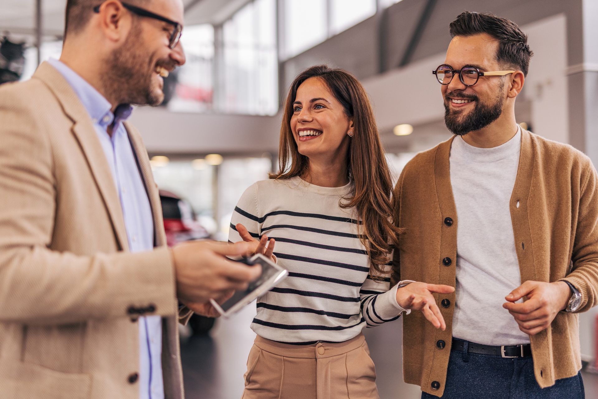 Car salesperson showing keys to a smiling couple in a dealership.