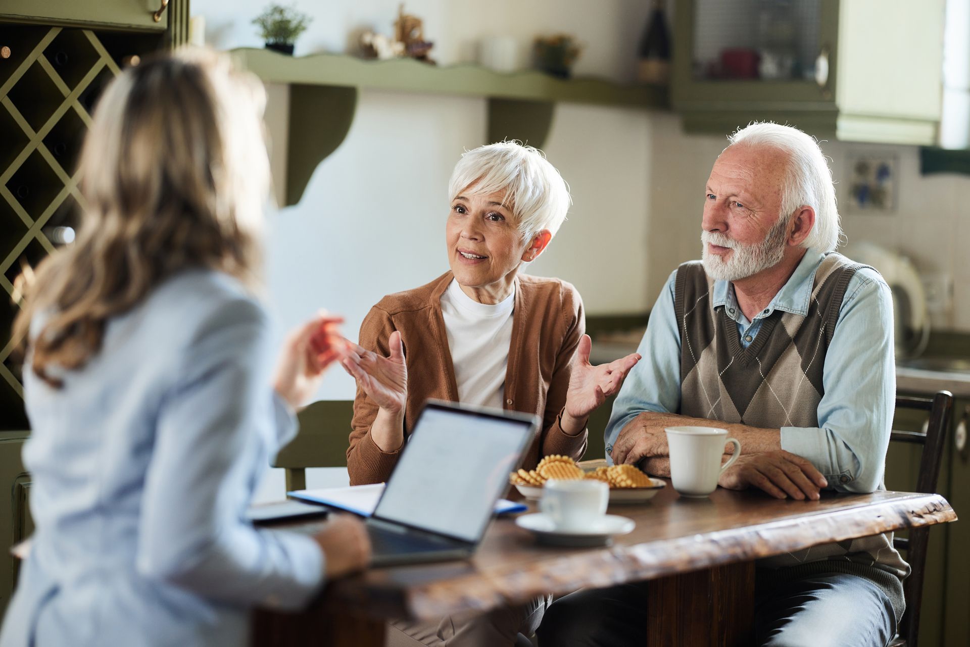 Woman with laptop consults with elderly couple at a kitchen table.
