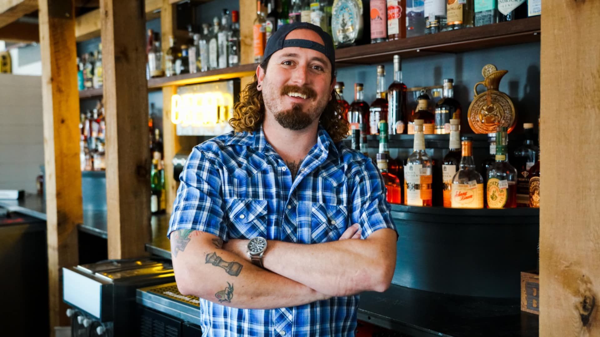 A man in a plaid shirt is standing in front of a bar.