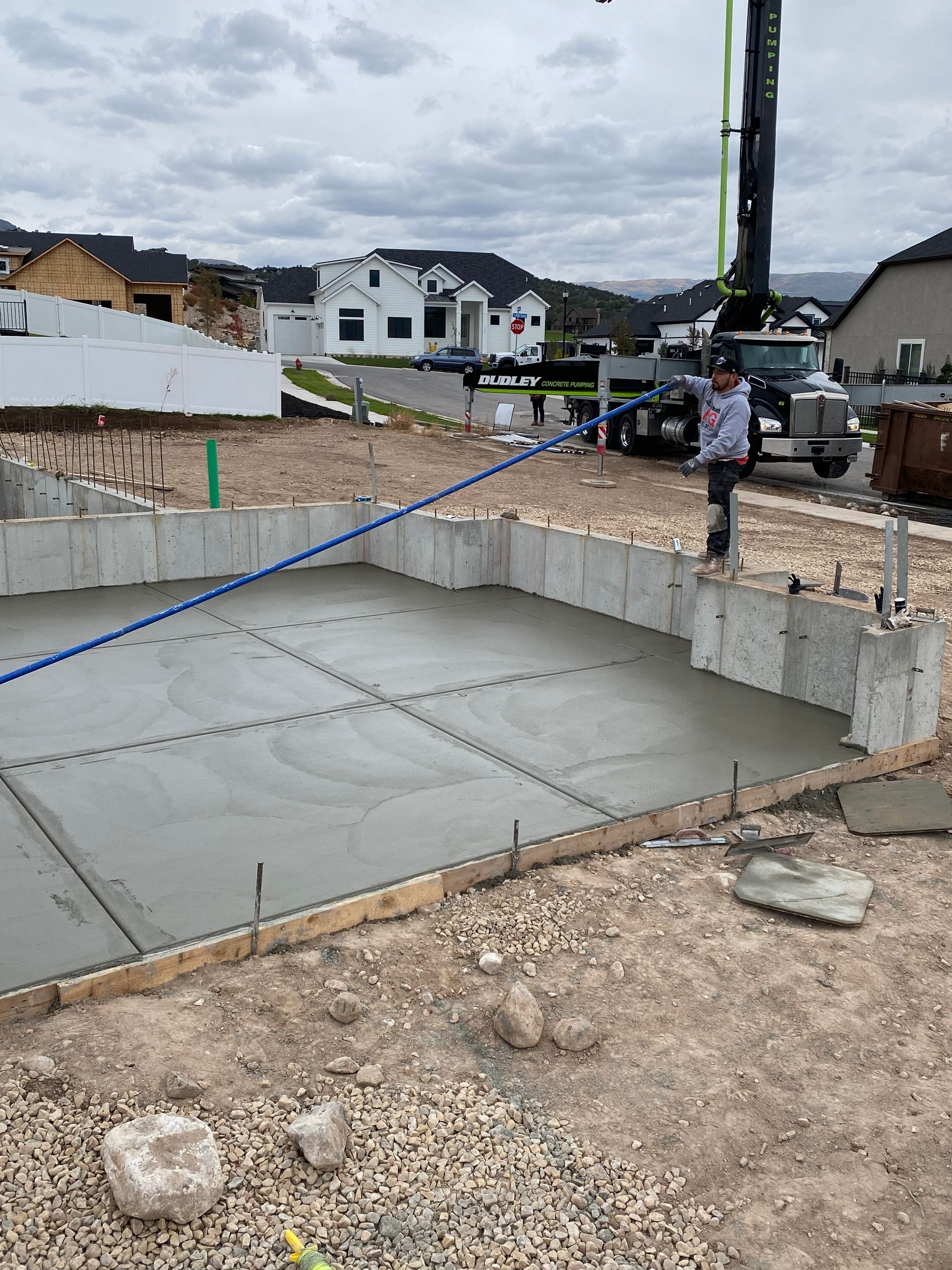 Freshly poured concrete foundation at a construction site with a worker and a concrete pump truck.