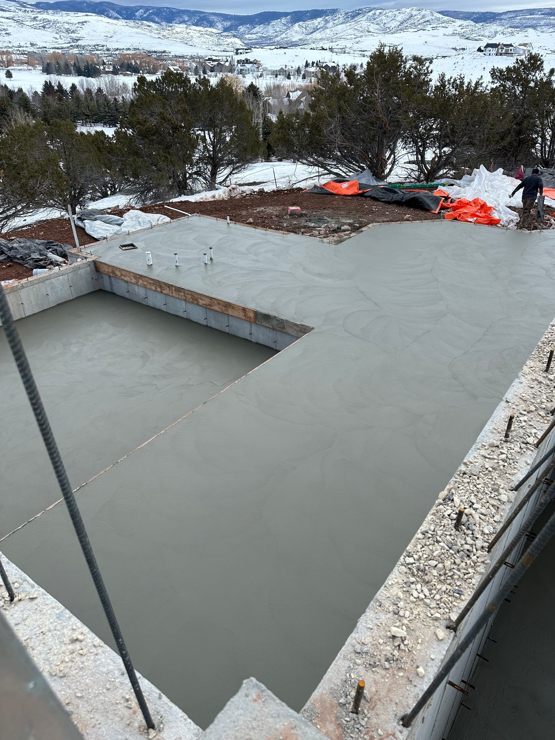Concrete foundation being poured; snowy mountain backdrop, construction site.