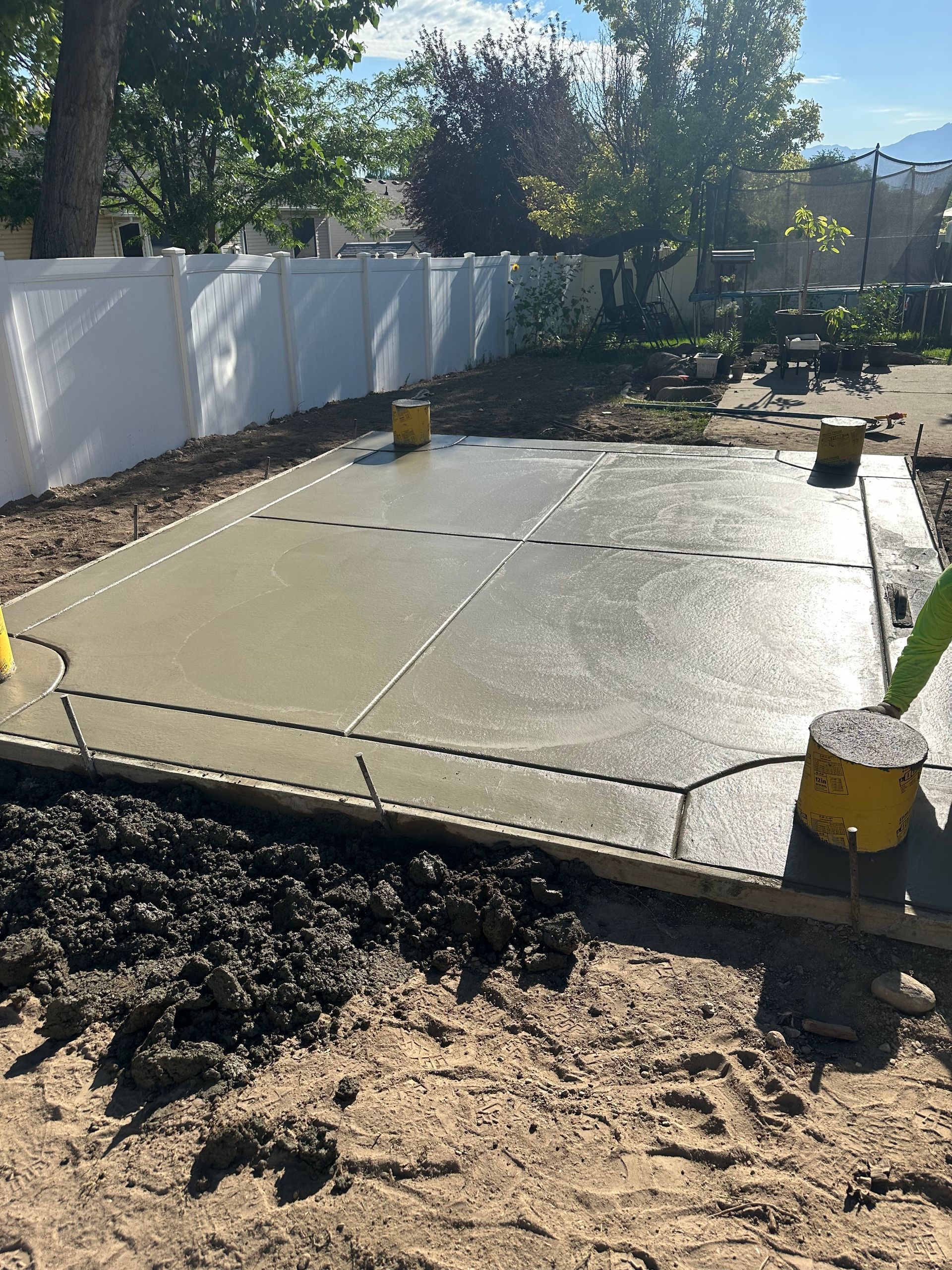 Newly poured concrete patio in a backyard setting, with wooden borders and yellow supports.
