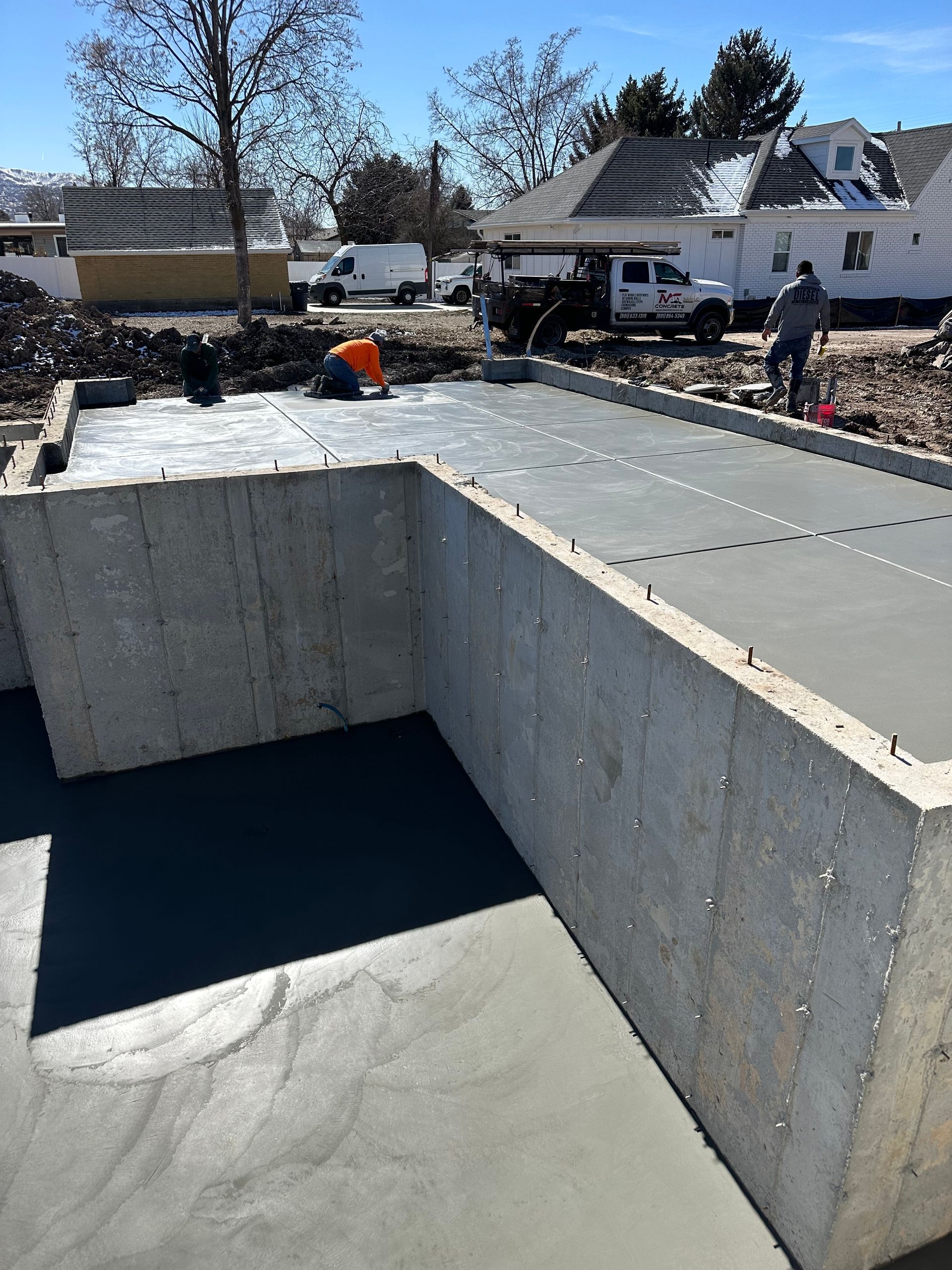 Concrete foundation construction site; workers smoothing concrete. 