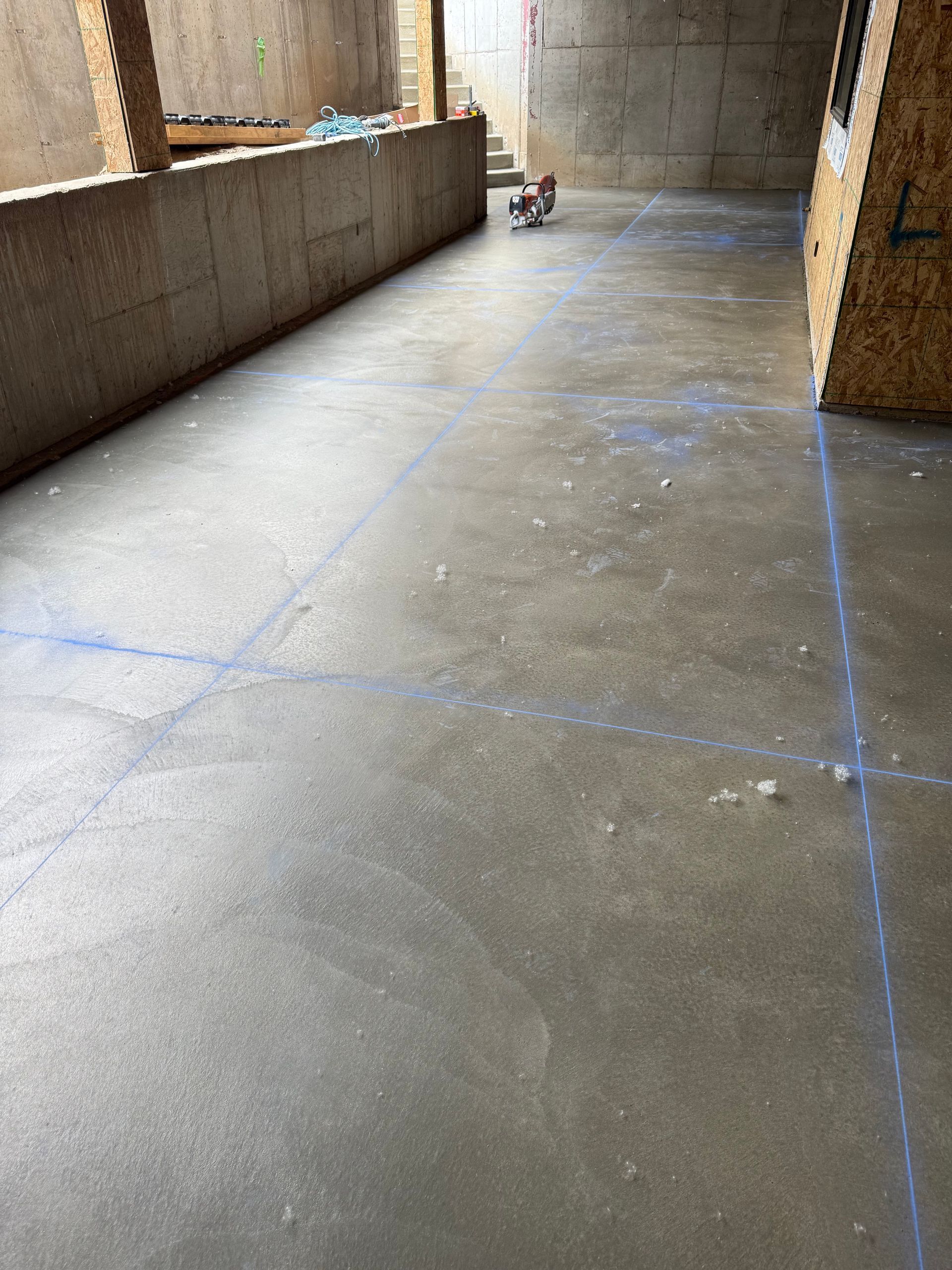 Concrete floor with blue chalk lines, under a building's exposed support structures.