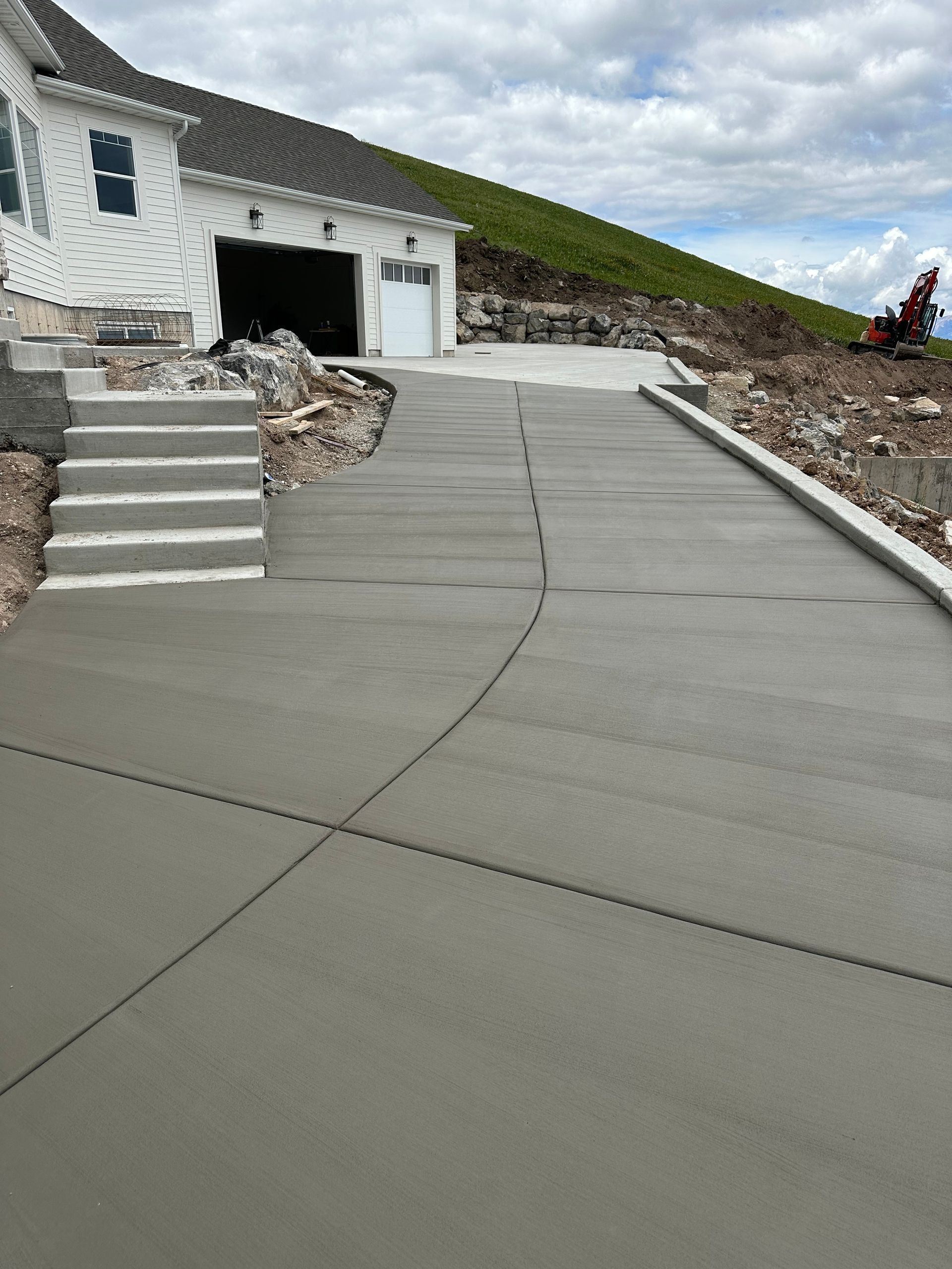 Newly poured concrete driveway leading to a white house with a garage and steps.