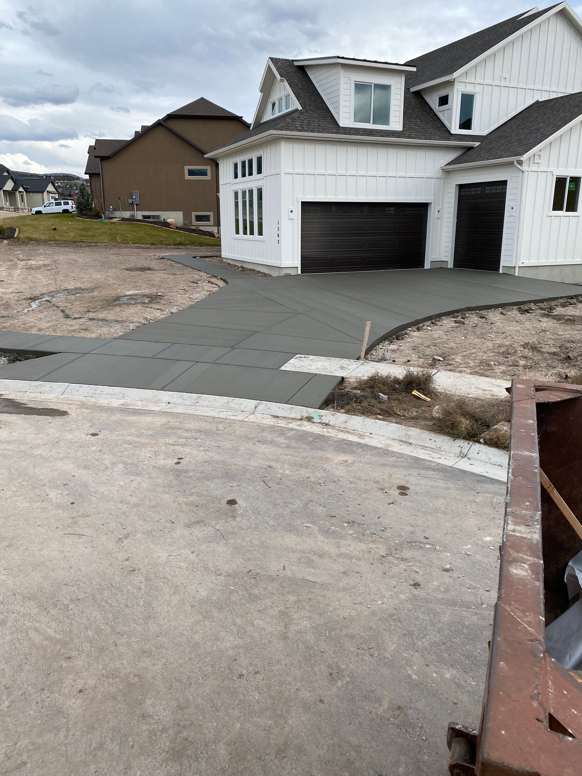 New concrete driveway poured at a white house under construction, on a cloudy day.