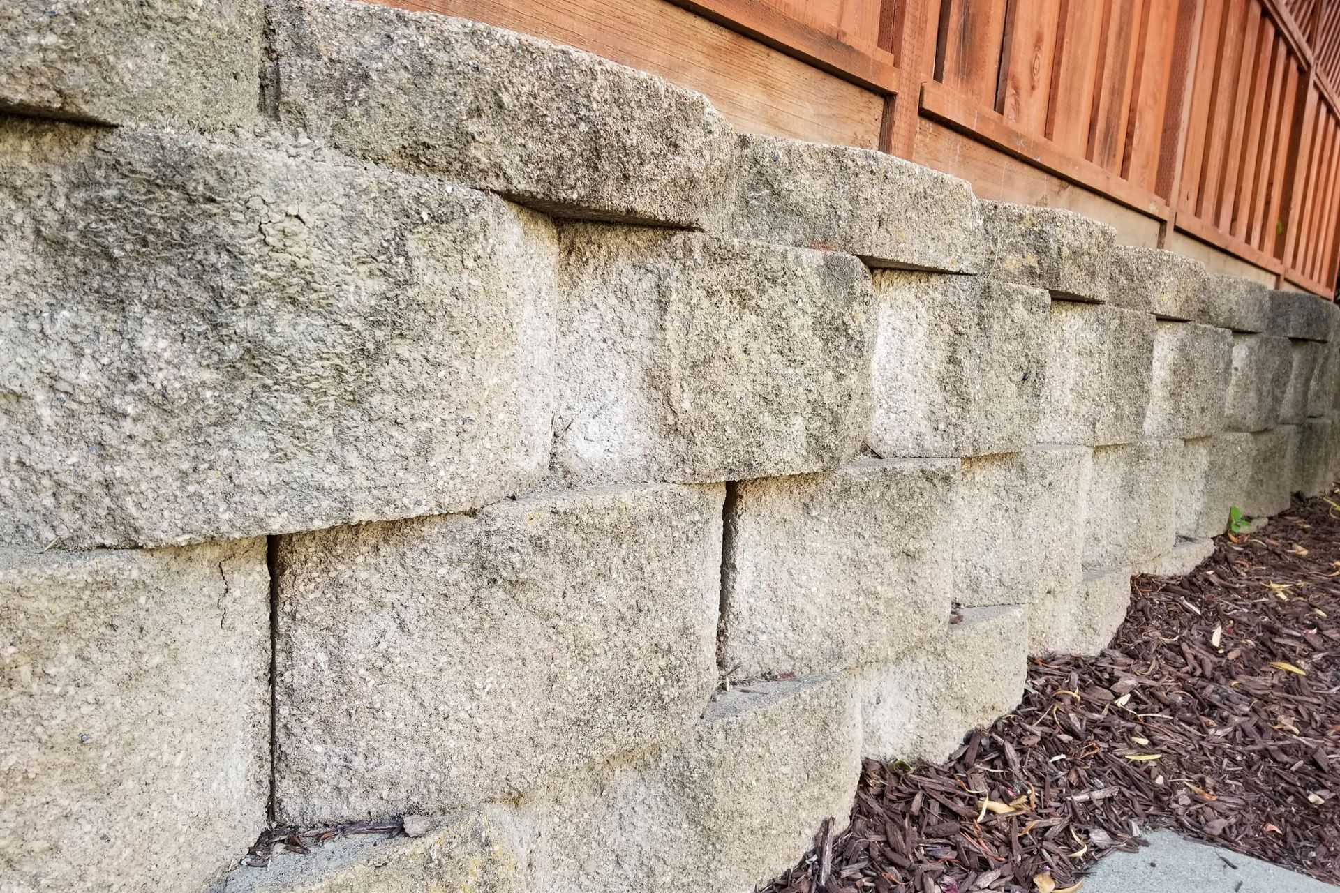 Gray stone retaining wall next to a wooden building, set in a bed of brown mulch.