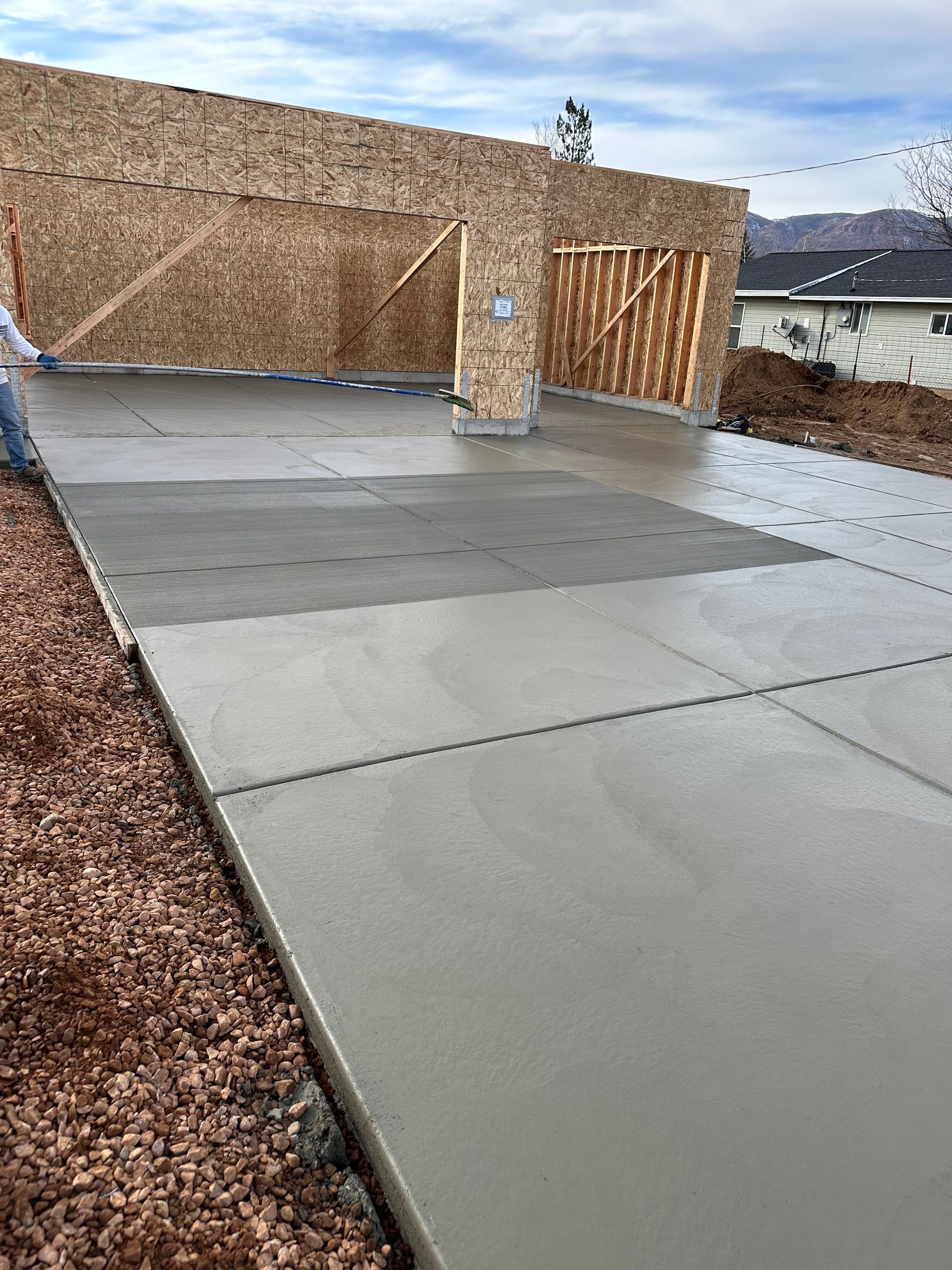 Newly poured concrete driveway and garage under construction, against a cloudy sky.