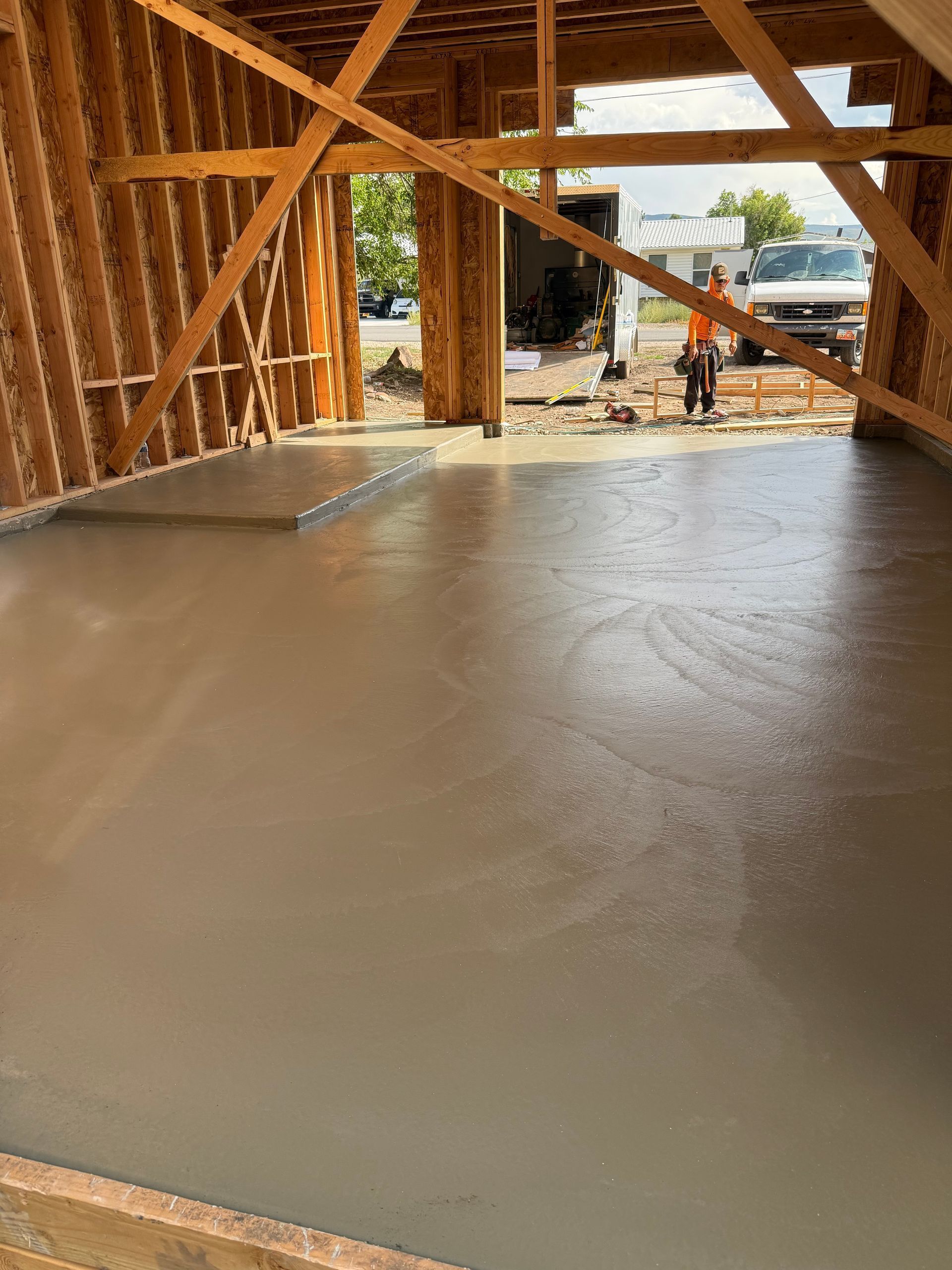 New concrete floor in a wooden framed building under construction, with a worker in the background.