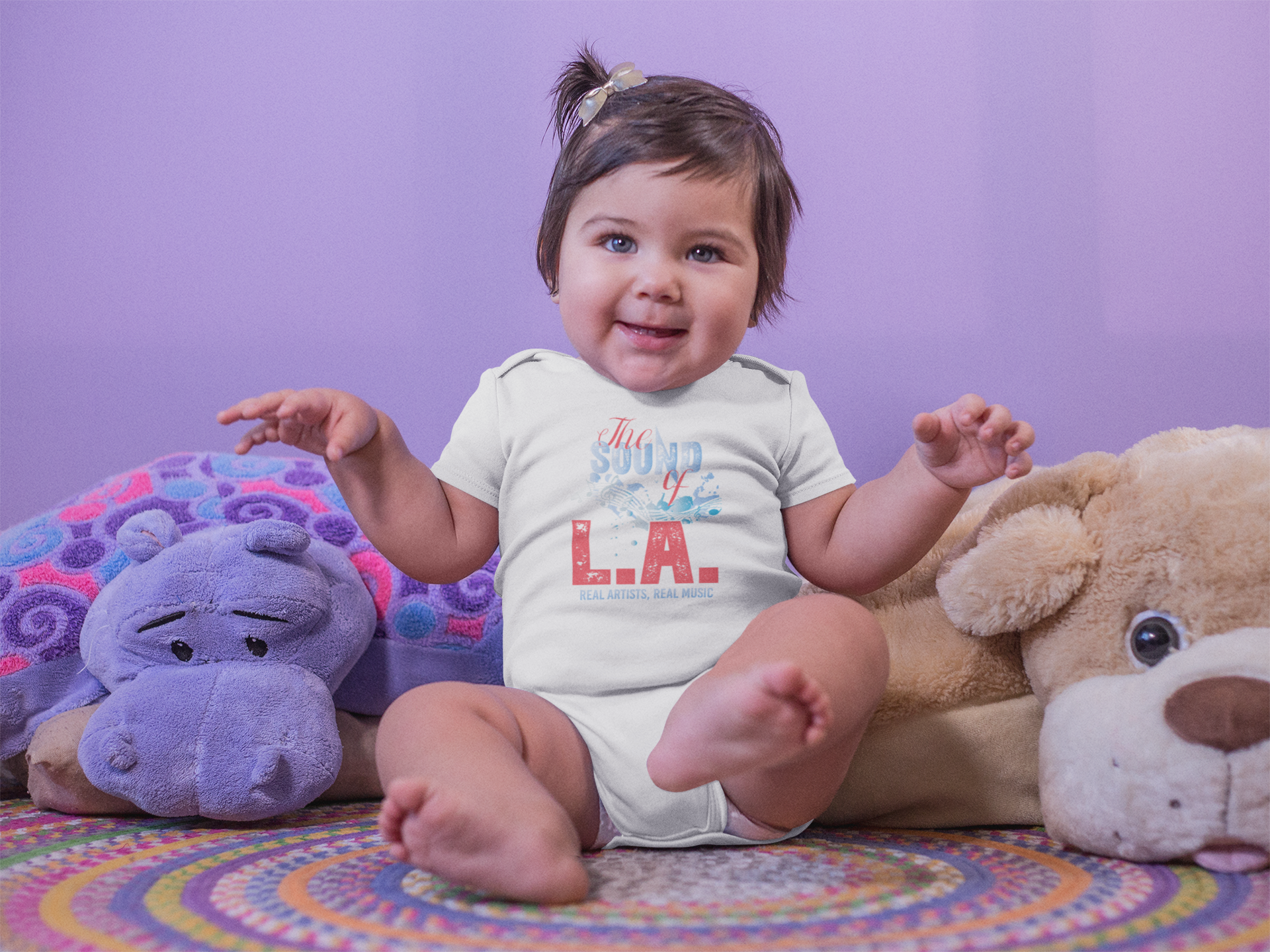 A baby is sitting on a bed next to stuffed animals.