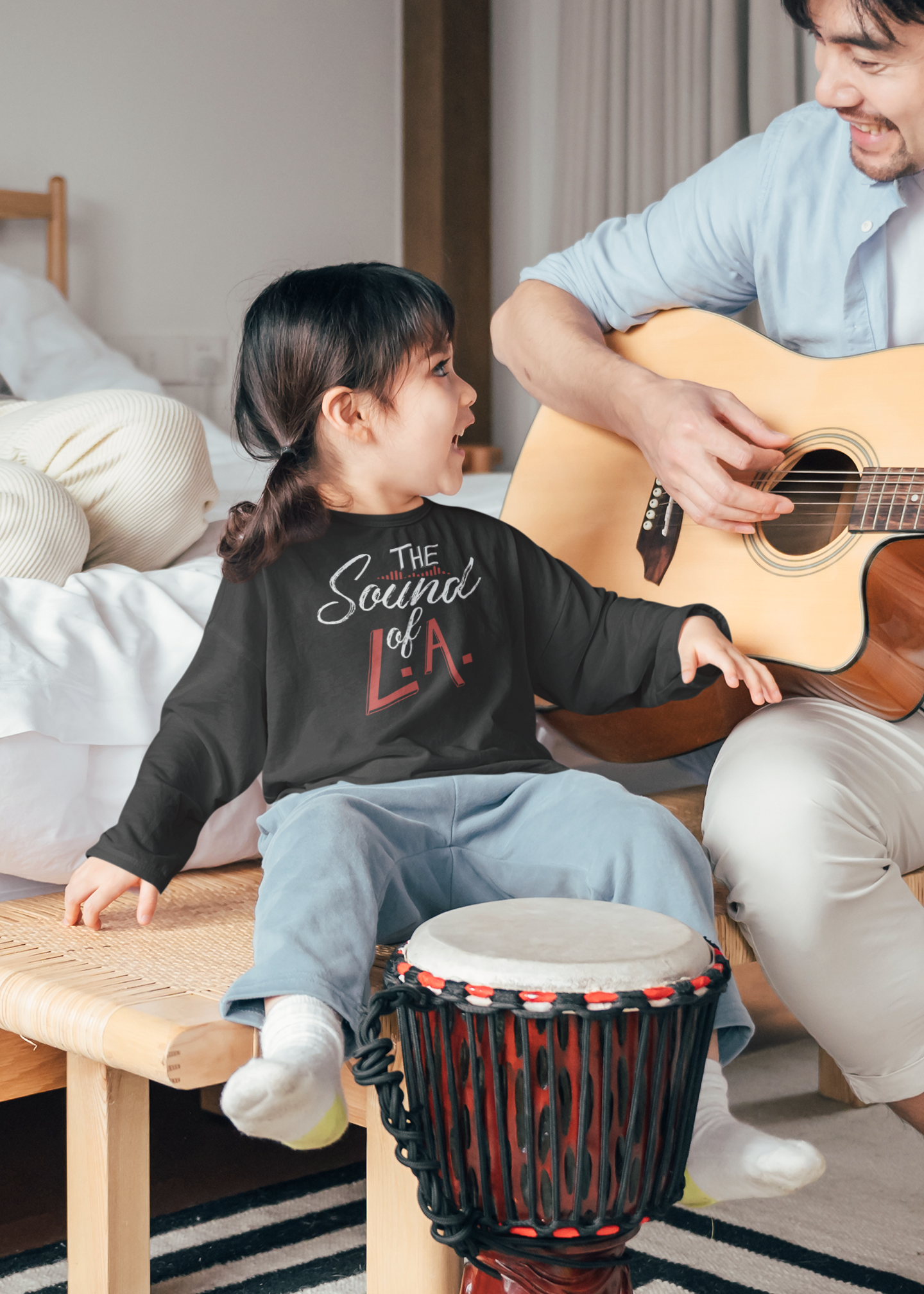 A little girl is sitting on a bench next to a man playing a guitar.