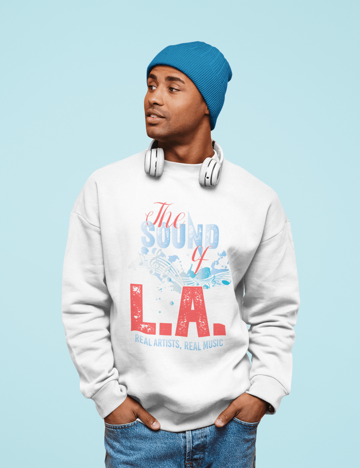 A man wearing a white sweatshirt and a blue hat is standing with his hands in his pockets.