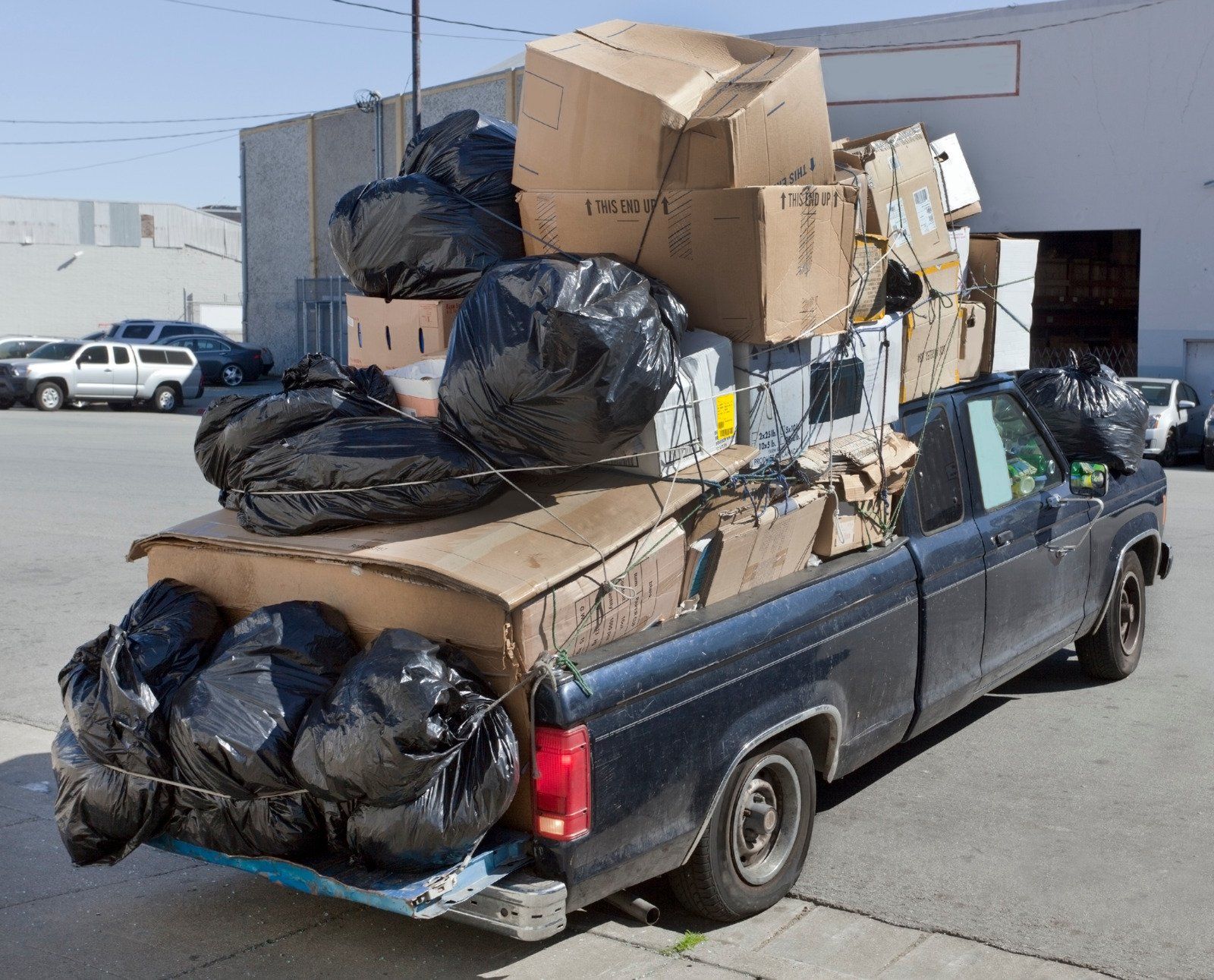 Pickup truck overloaded with garbage bags and boxes.