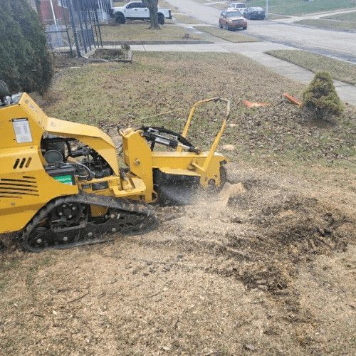 A yellow stump grinder is cutting a tree stump in a yard.