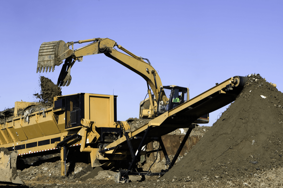 An excavator is loading dirt into a conveyor belt.