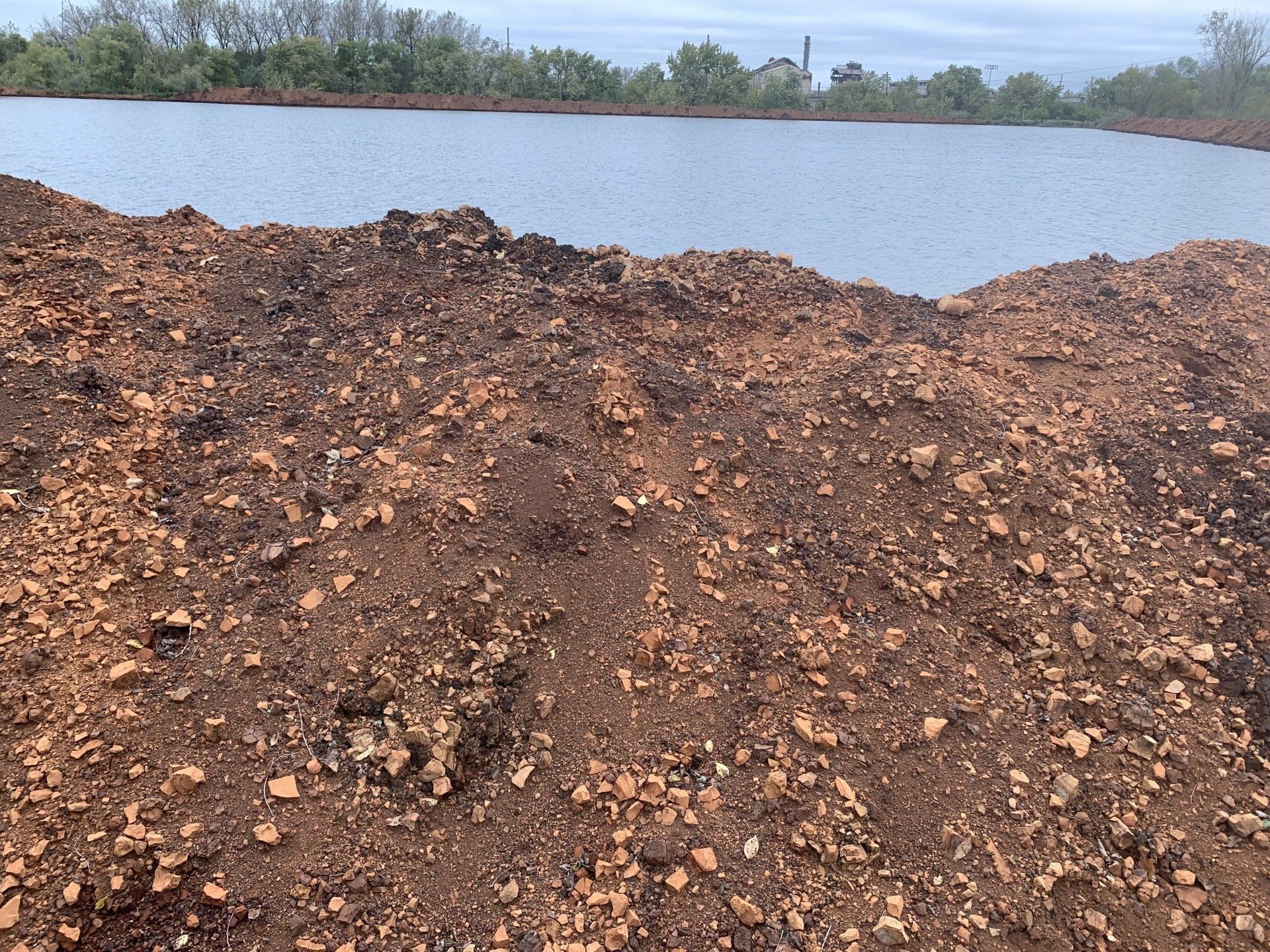 A large pile of dirt is sitting next to a body of water.