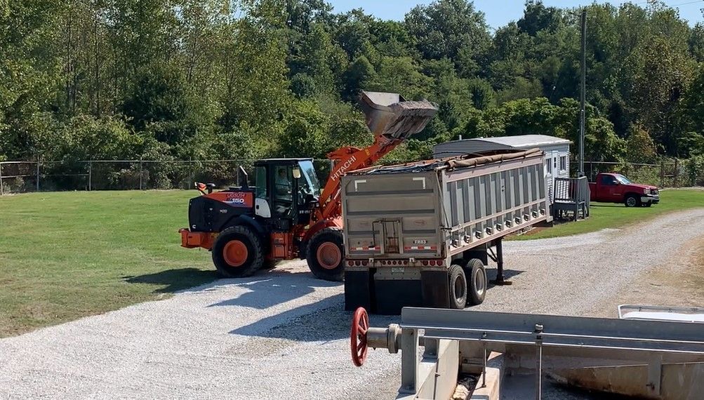 A dump truck is being loaded with gravel by a bulldozer.