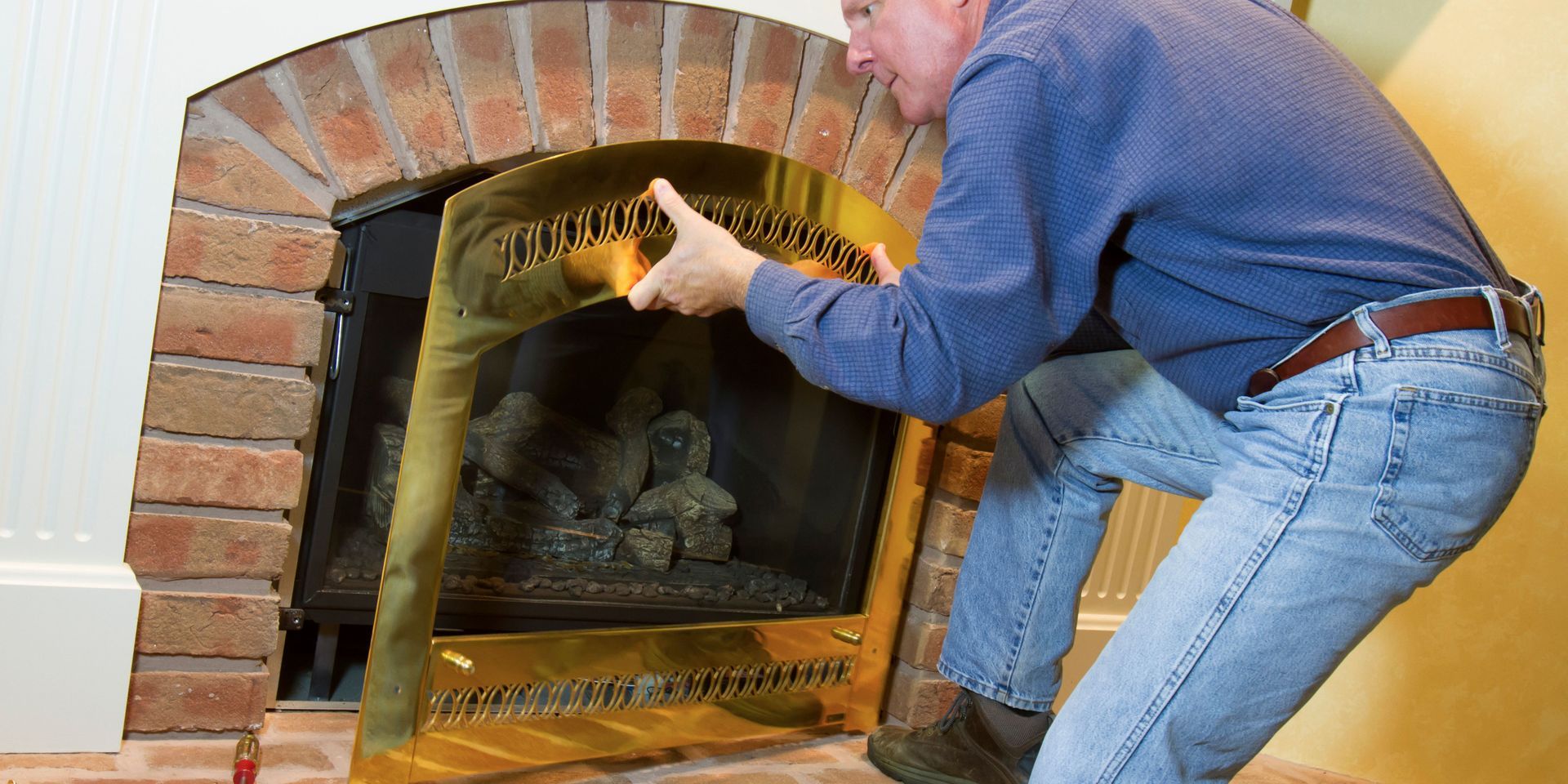 Man installing a golden fireplace screen into a brick hearth.