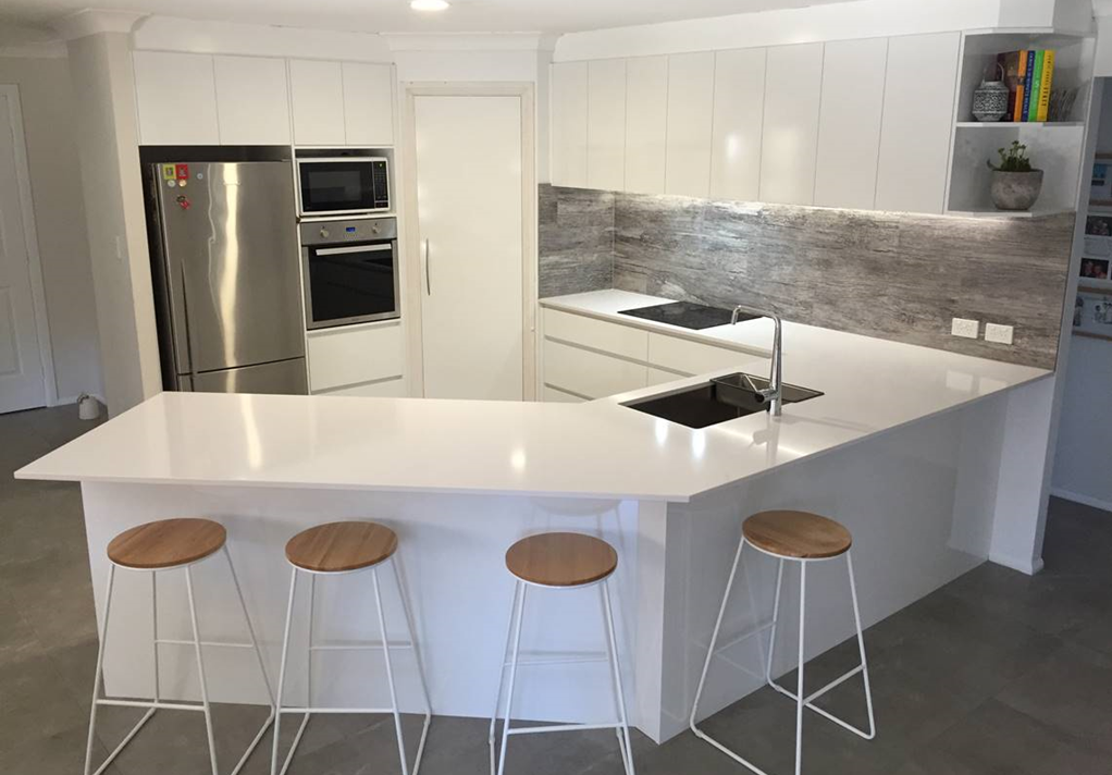 Modern white kitchen with island, stainless steel appliances, and wooden stools. — Kitchens Factory Direct in Port Macquarie, NSW