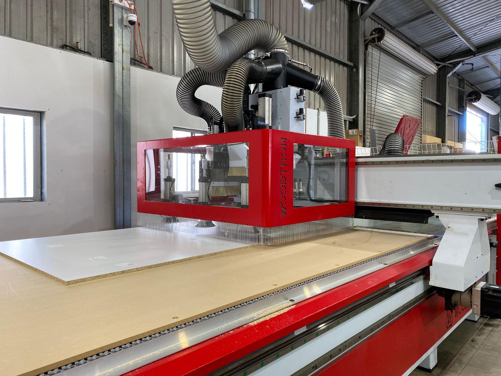 A red CNC machine cutting a large wooden panel in a workshop. - Kitchens Factory Direct in Port Macquarie, NSW