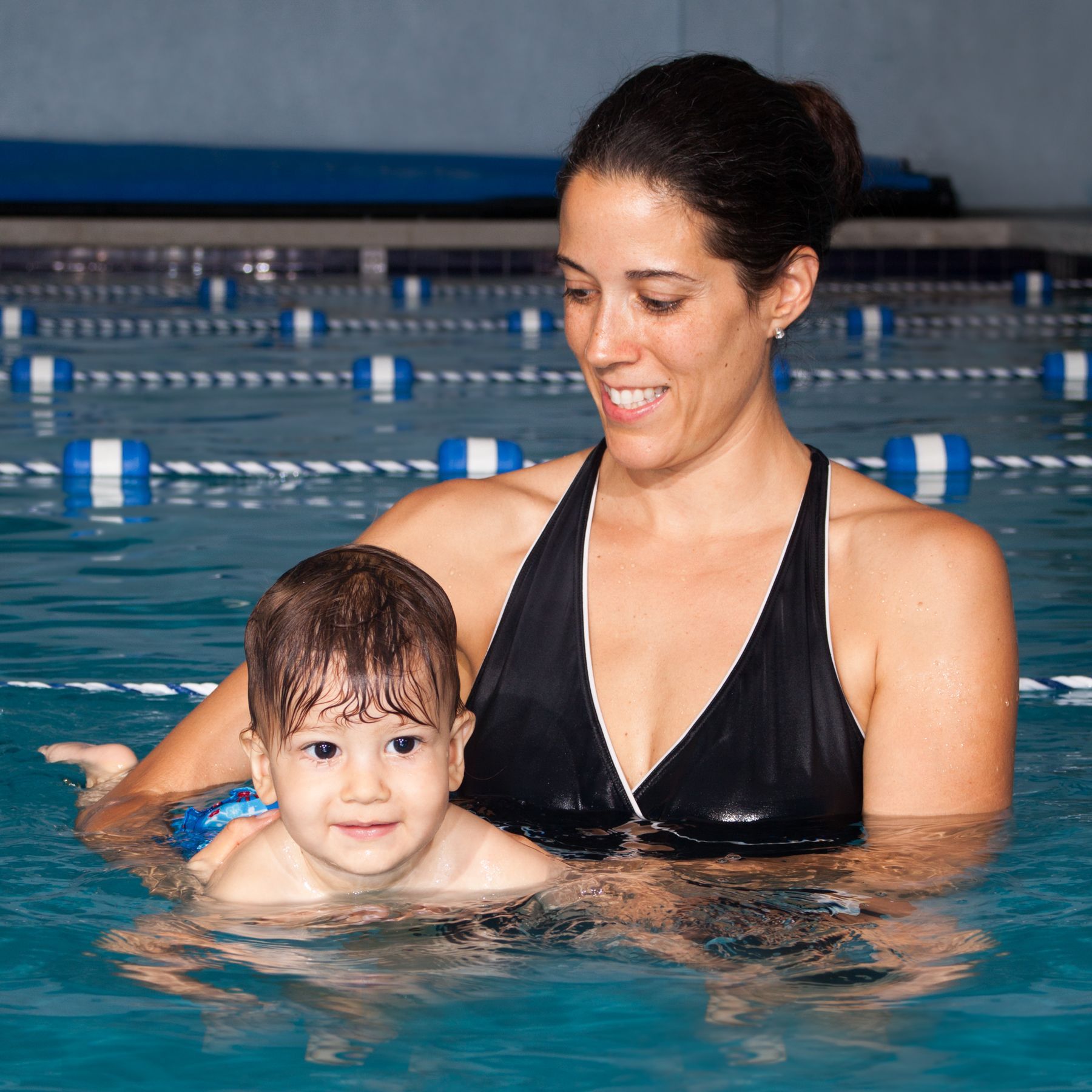 a woman is holding a child in a swimming pool for a swim school