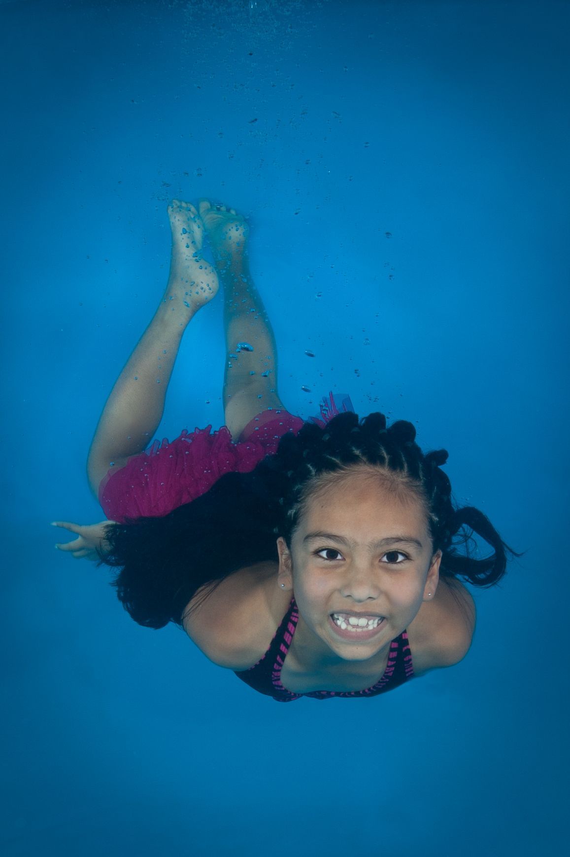 a little girl is swimming underwater in a pool during swim lessons.