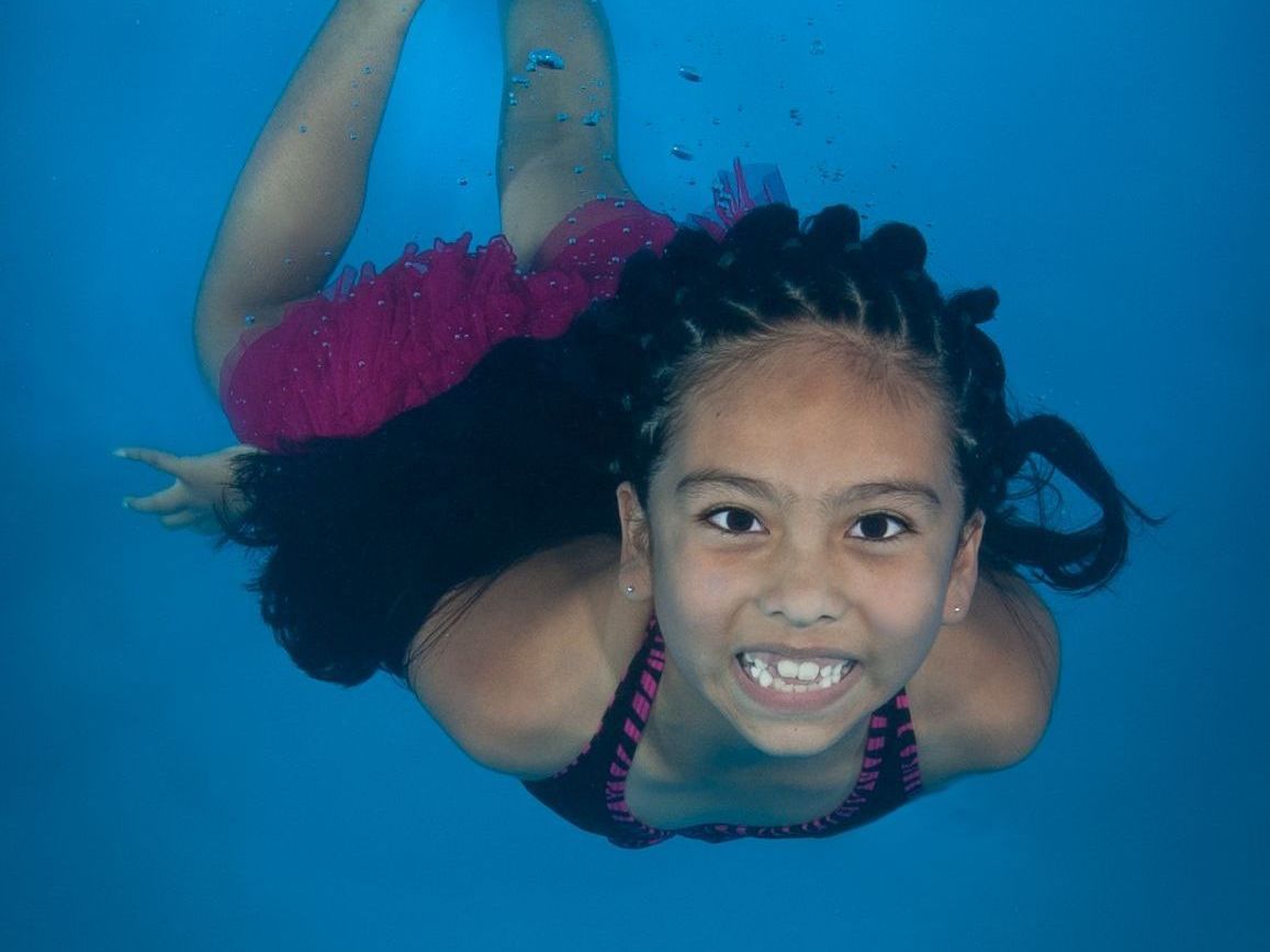 girl swimming underwater smiling during swim lessons